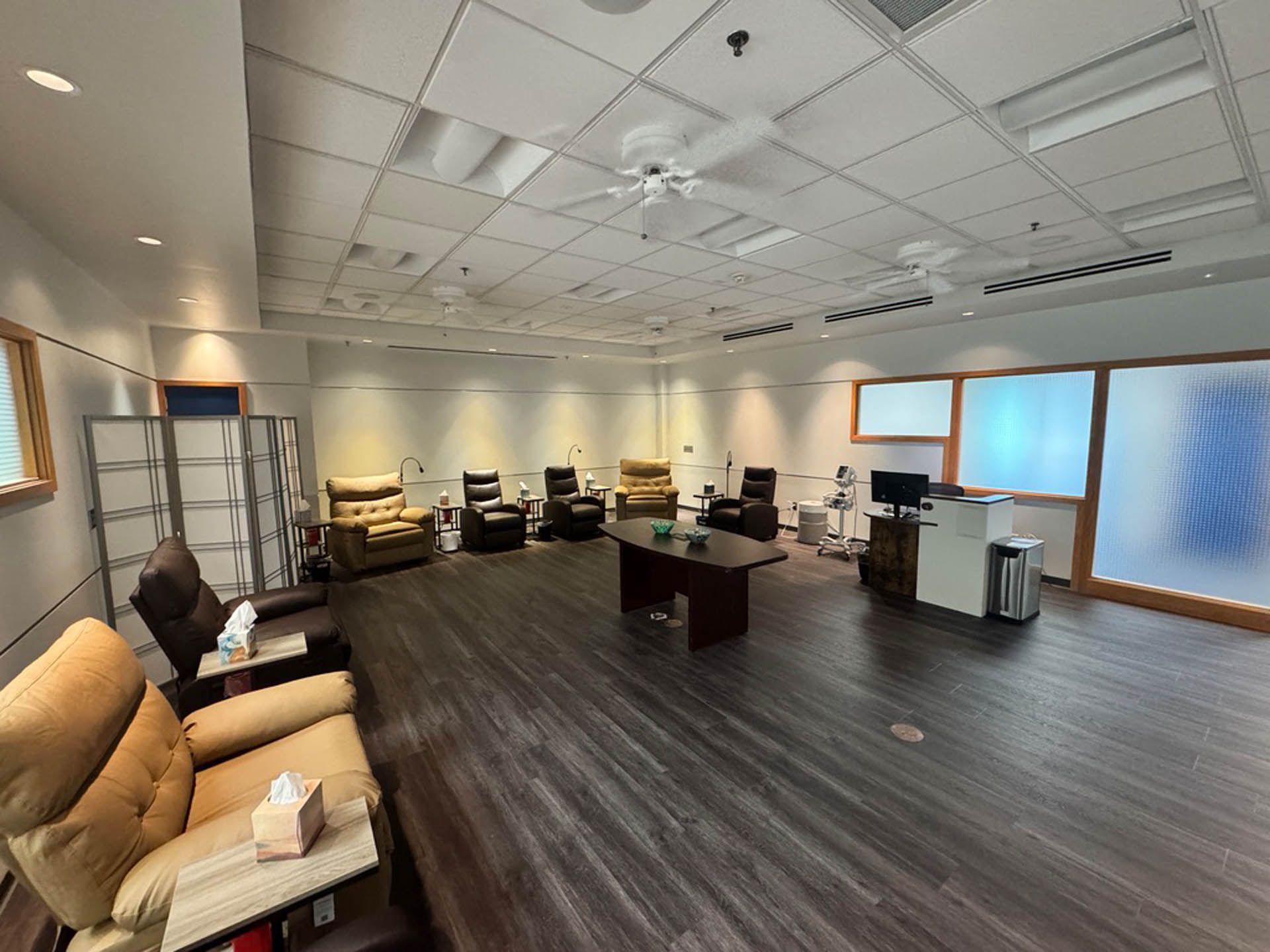 Awaiting room with recliners, coffee table, and frosted windows. Gray walls and ceiling, dark wood floor.