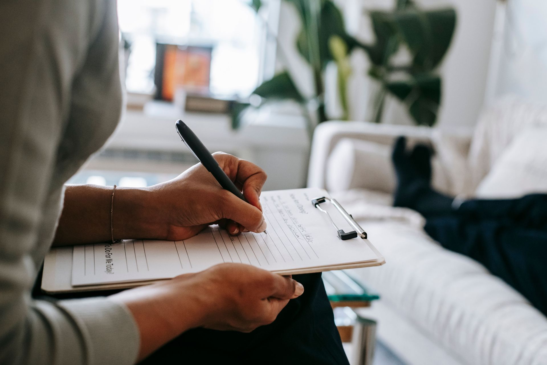 Person writing in a notebook on a couch in a bright living room