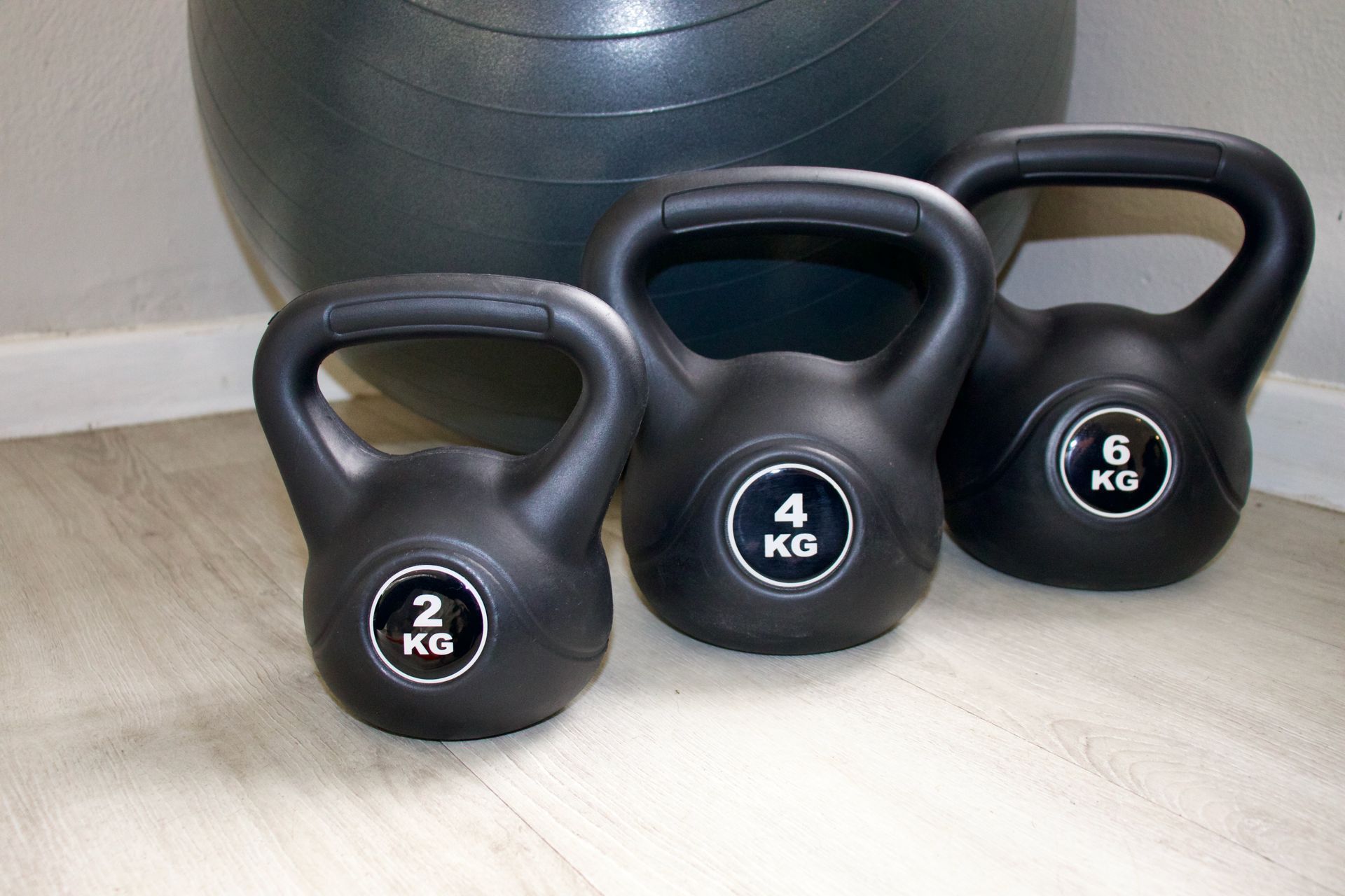 Three black kettlebells of varying weights: 2kg, 4kg, and 6kg, in front of an exercise ball.