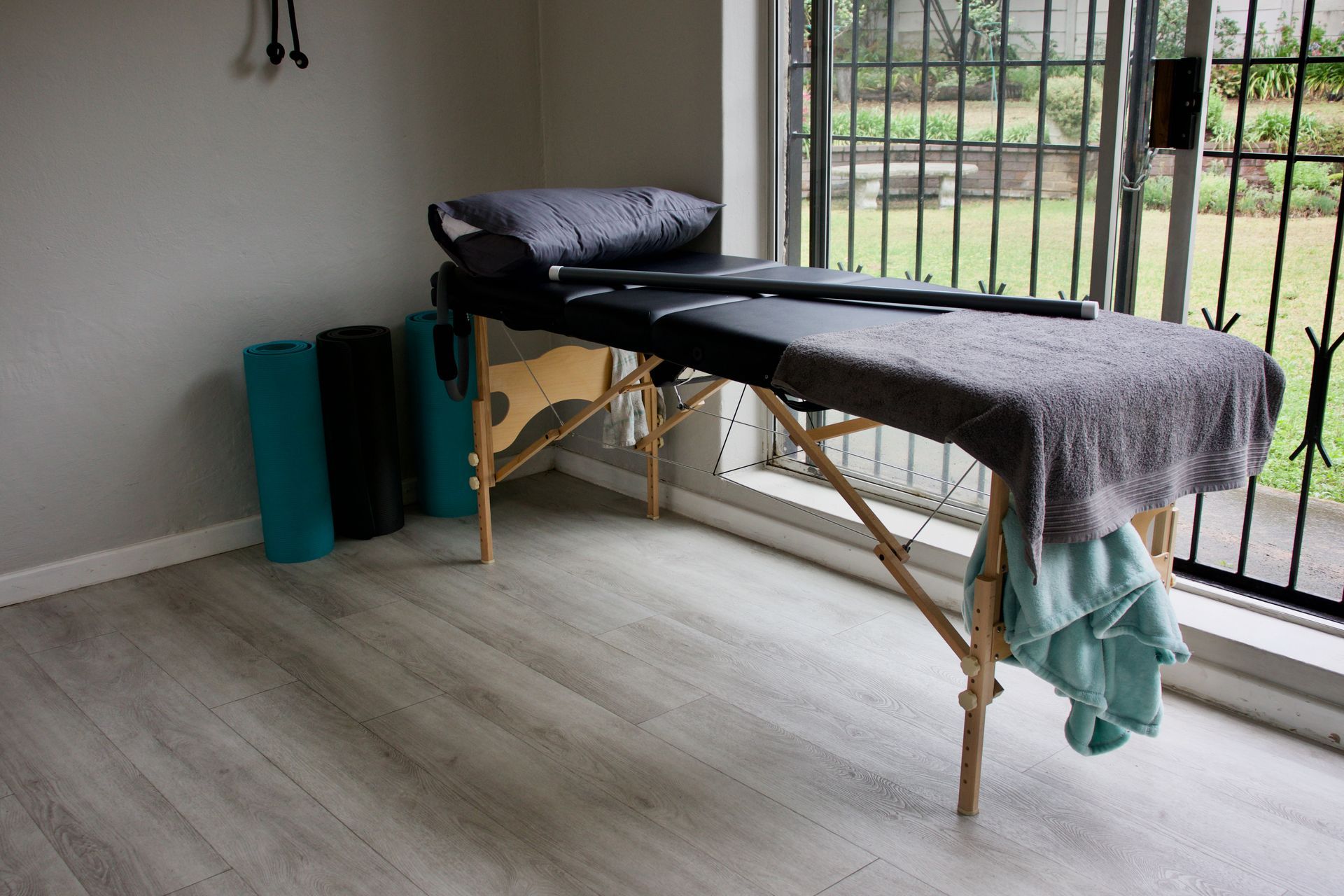 Massage table in a room with exercise mats and a window overlooking a garden.