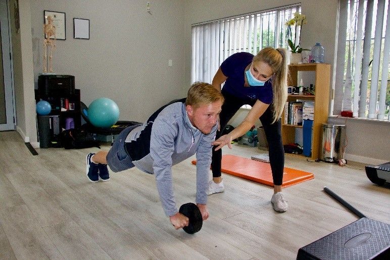 A man doing an ab roll-out exercise with guidance from a woman in a gym.