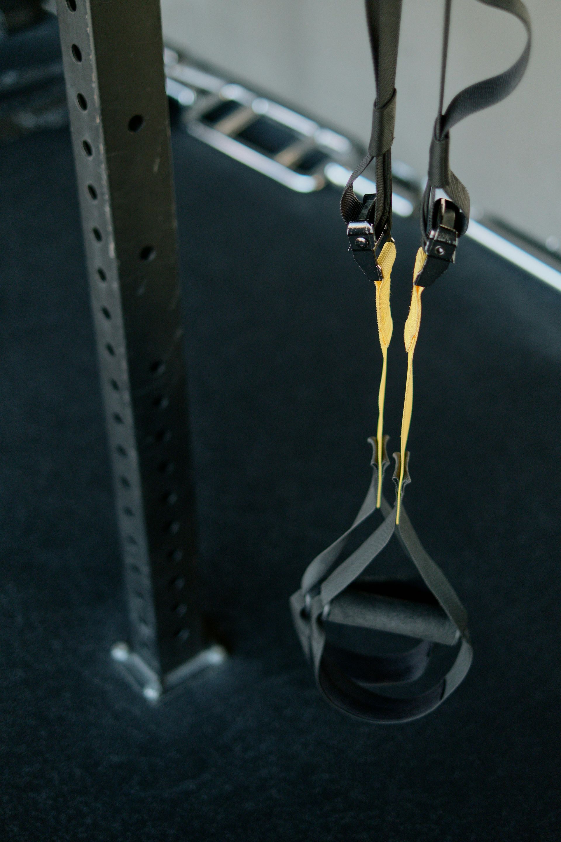 Black exercise straps hanging from a metal support frame against a dark surface.