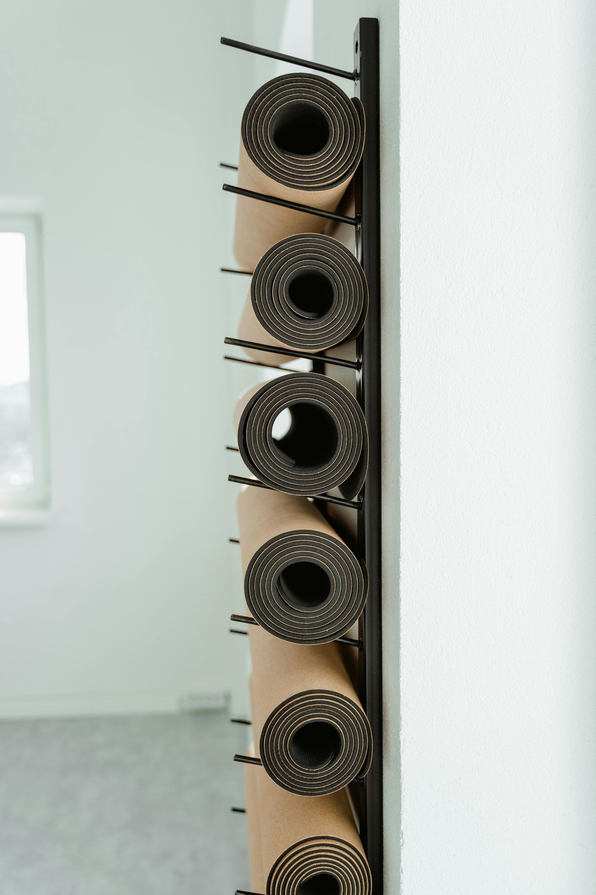 Black metal rack holding rolled-up yoga mats against a white wall in a room.