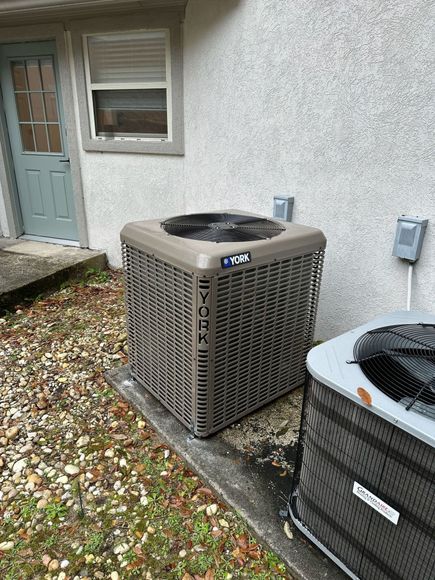 Two air conditioners are sitting next to each other on the side of a house.