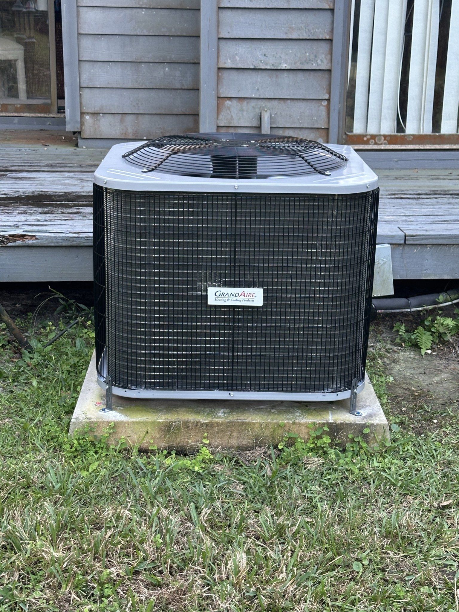 A large air conditioner is sitting in the grass in front of a house.