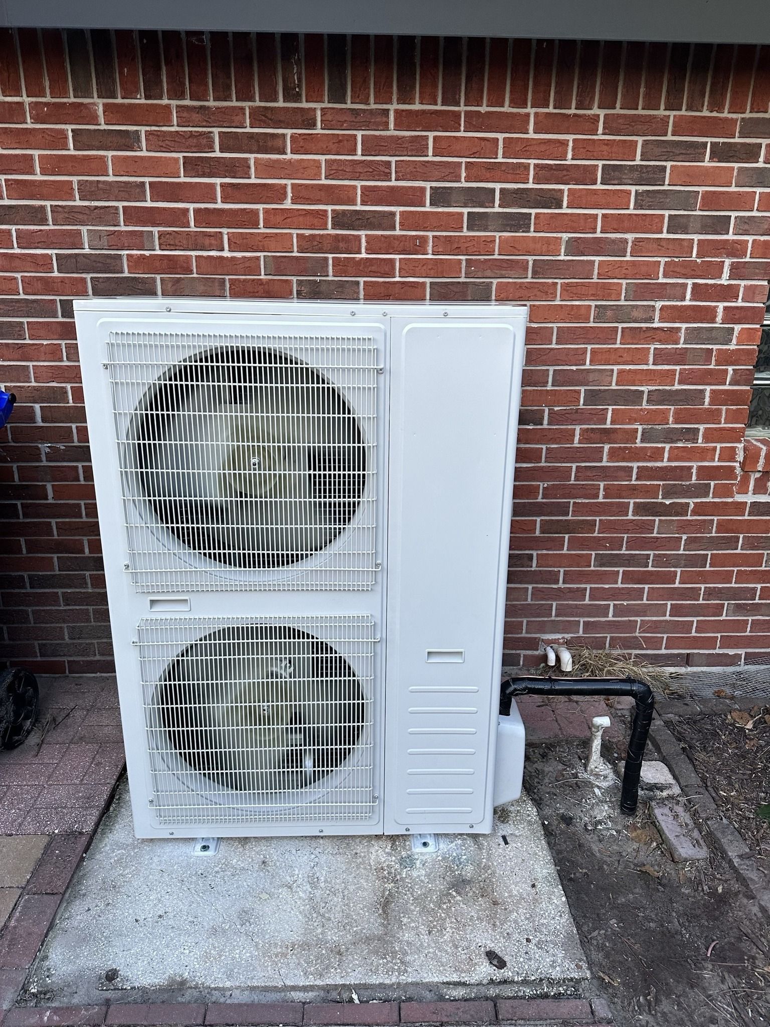 A white air conditioner is sitting in front of a brick wall.