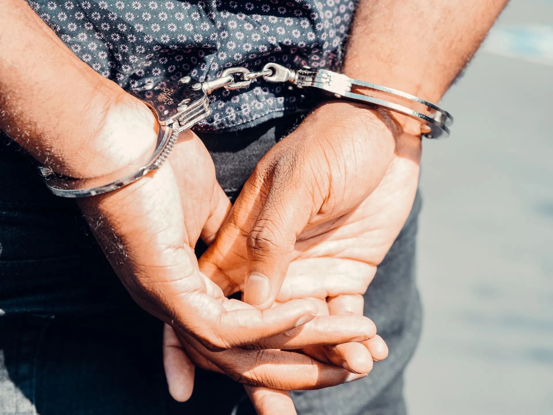Person's hands cuffed behind their back. Silver handcuffs, dark shirt, partial view.