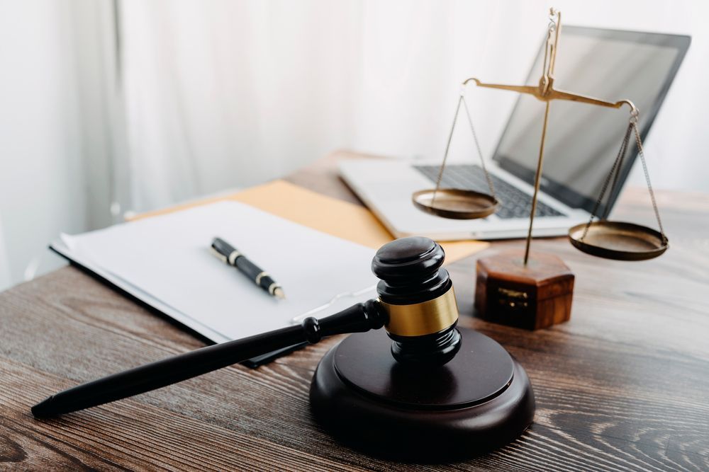 Wooden gavel, scales of justice, laptop, and documents on a desk, symbolizing law and justice.