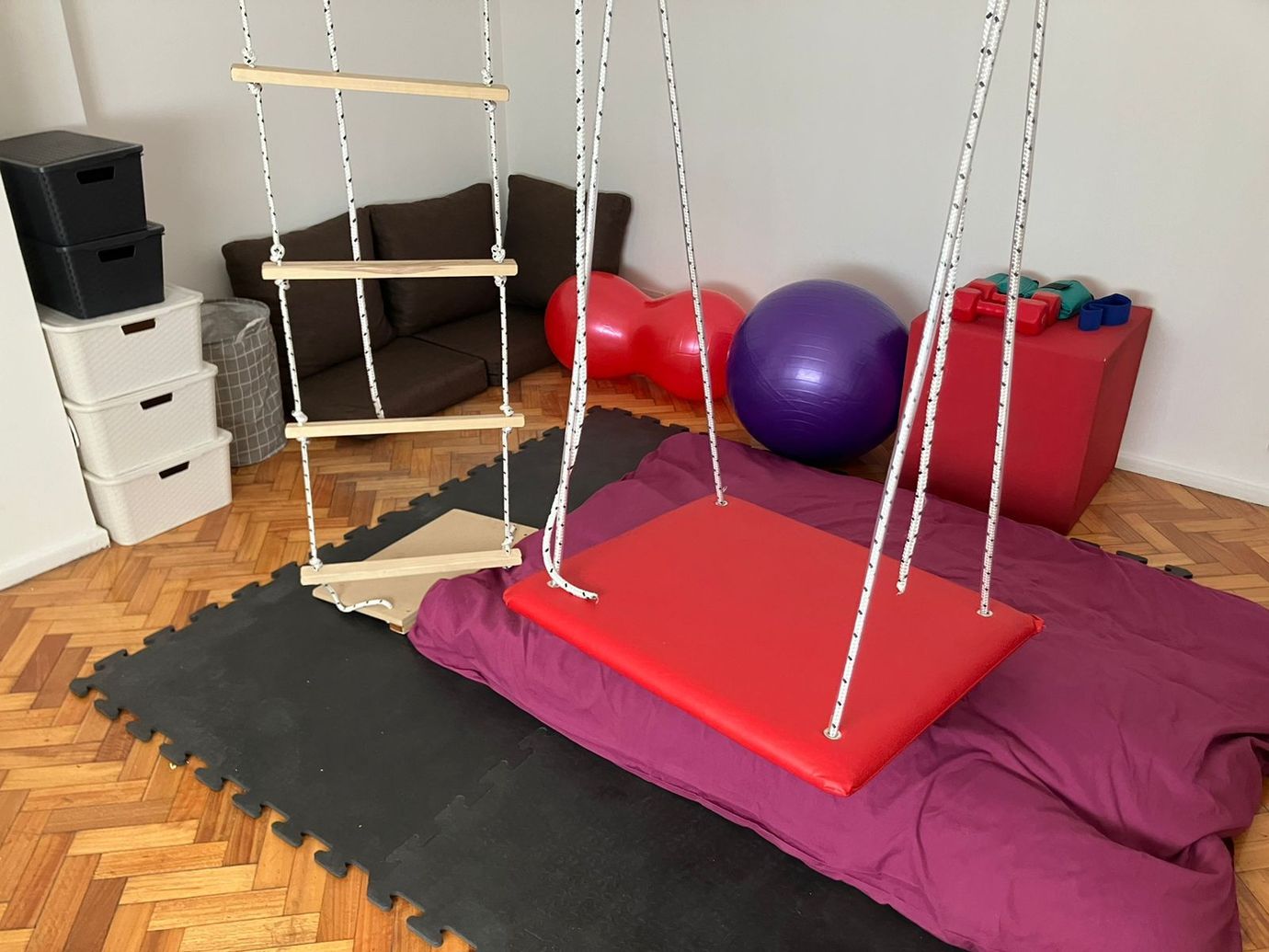 Sobre un suelo de parqué de madera, una mesa blanca con dos sillas de metal blancas y una batería electrónica en una esquina.