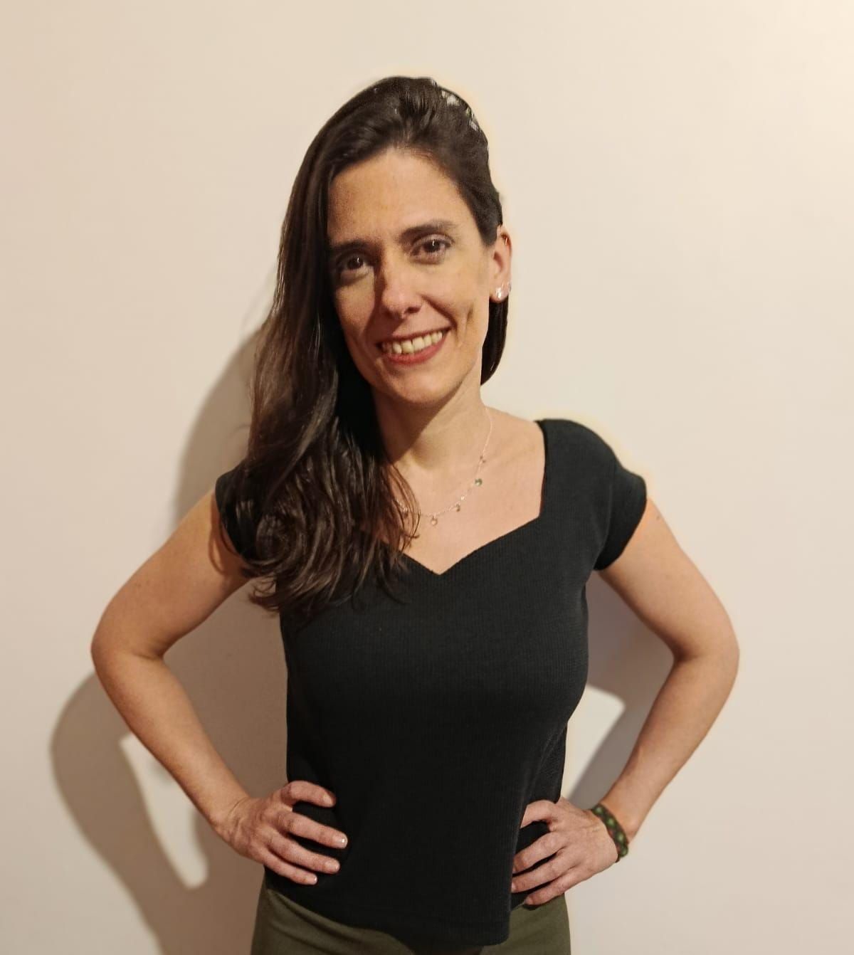 Una persona con cabello largo castaño, vestida con una blusa negra con escote en V.