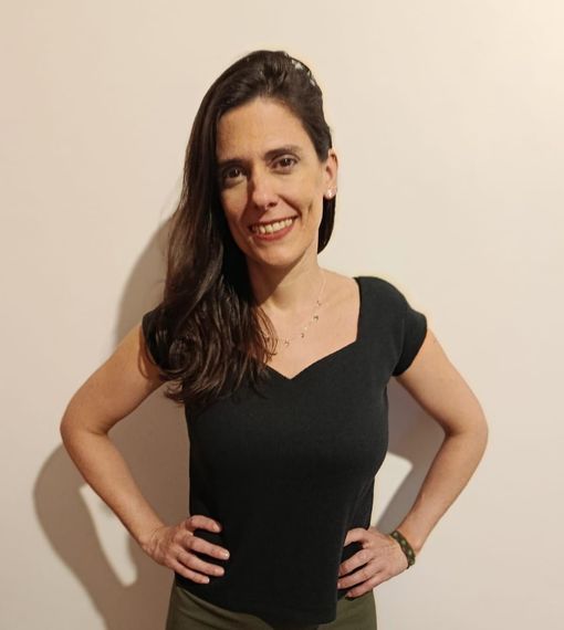 Una persona con cabello largo castaño, vestida con una blusa negra con escote en V.