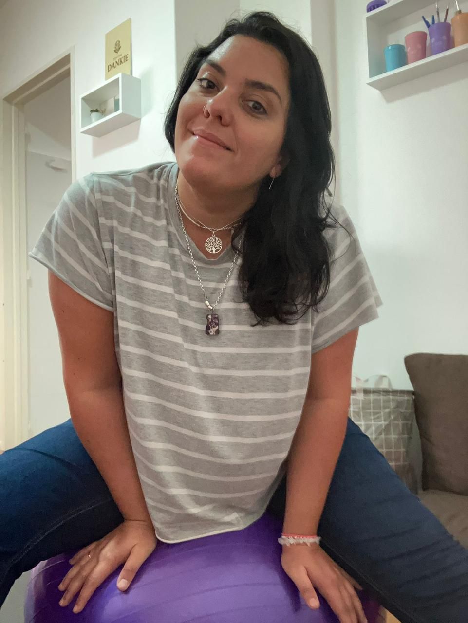 Una persona de cabello oscuro lleva una camisa de rayas grises y blancas y collares.