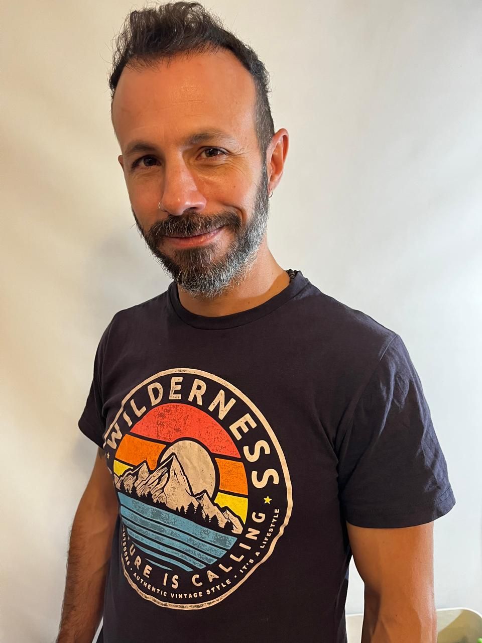 Una persona con barba, que lleva una camiseta azul marino con el dibujo de una montaña al atardecer, mira hacia la cámara.