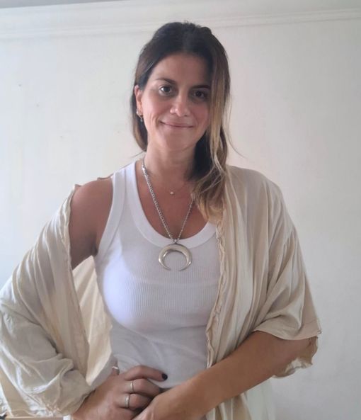 Una persona sonriente con una camiseta blanca sin mangas, un cárdigan beige abierto.