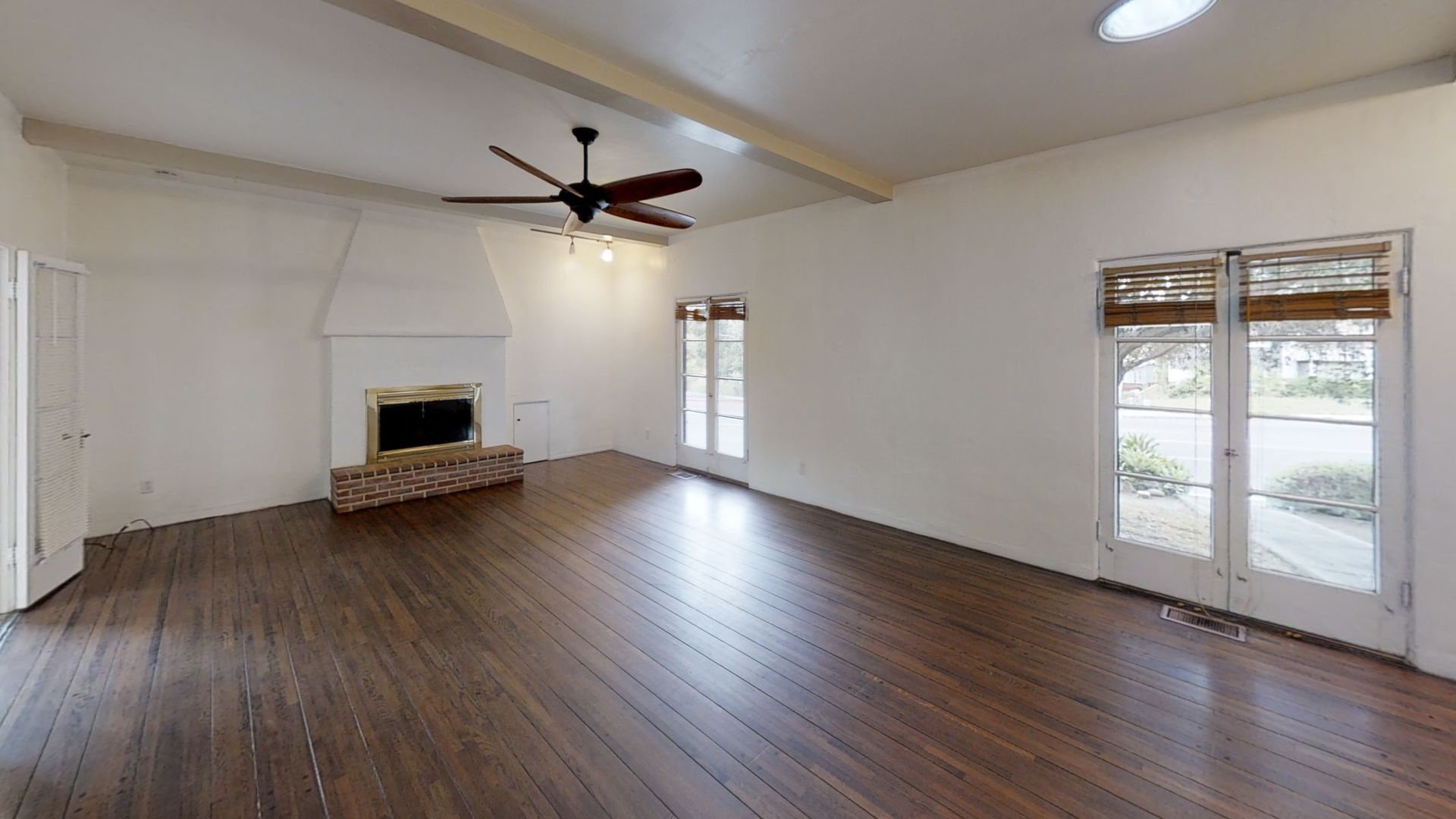 Empty living room with hardwood floors, fireplace, and french doors.