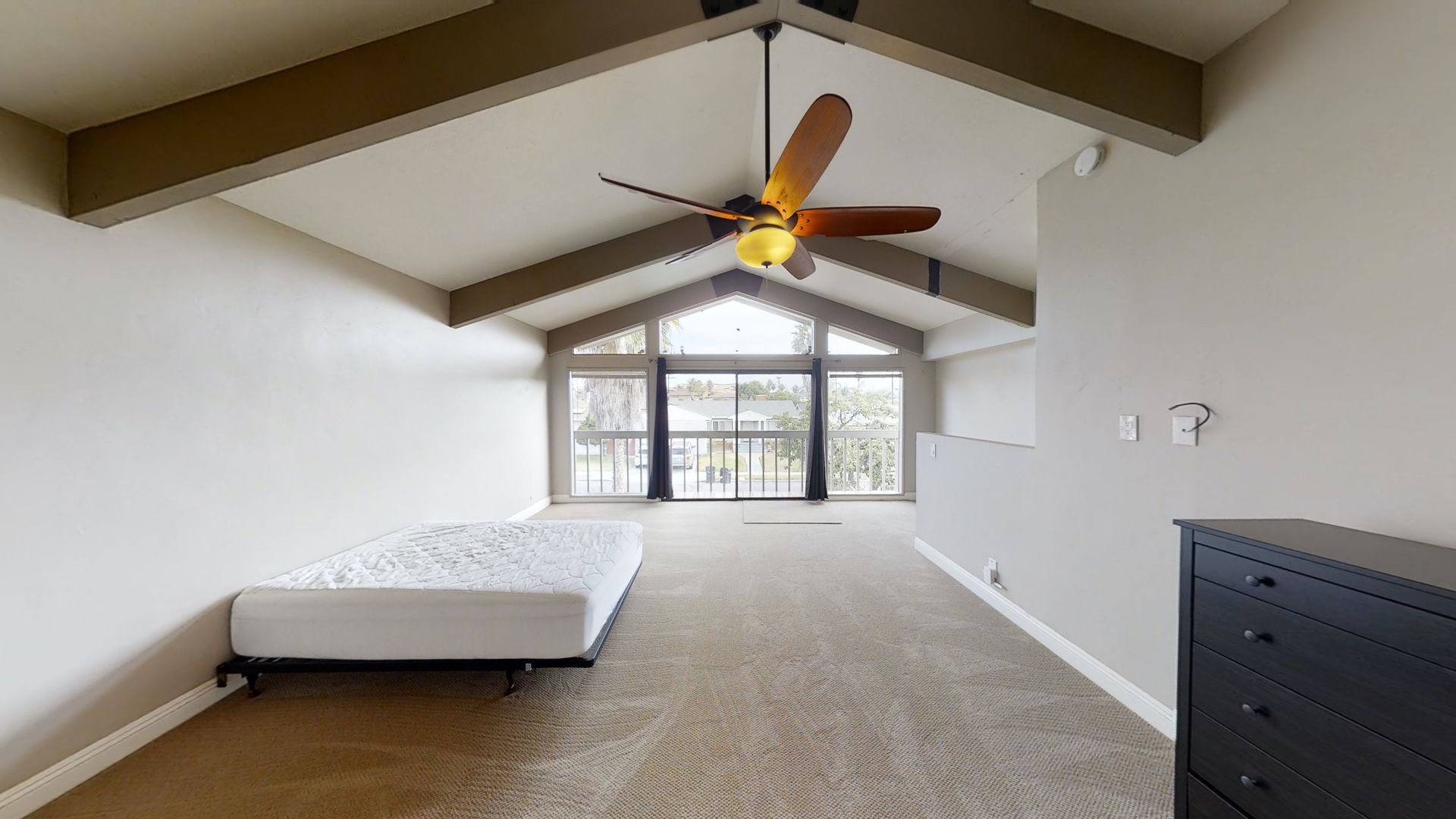 Spacious room with high, angled ceiling, large windows, a bed, and a dresser.