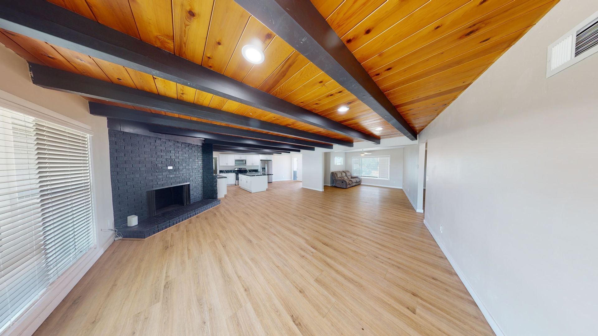 Wooden-floored living room with a black fireplace, wooden ceiling, and large windows.