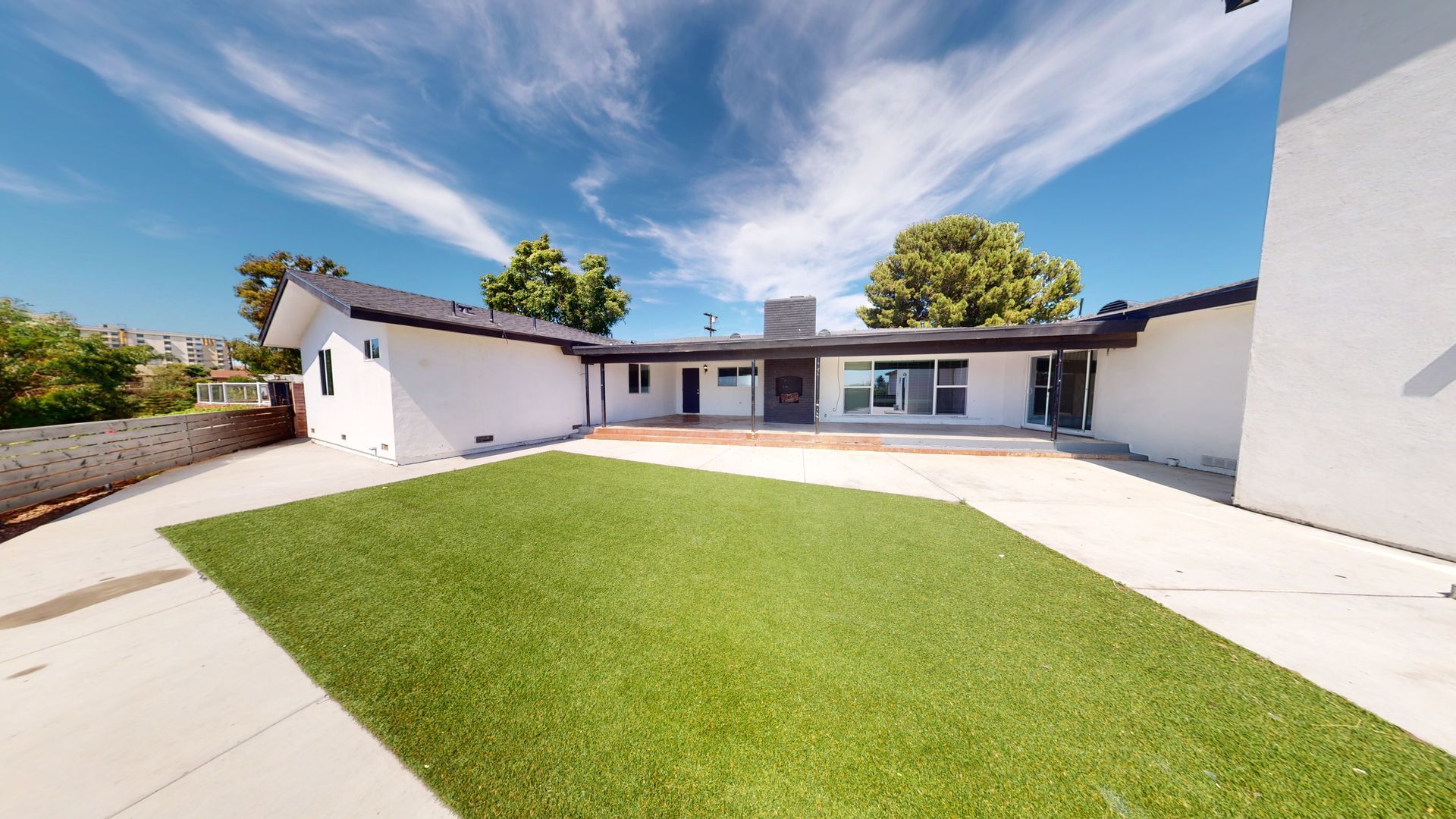 Exterior view of a white house with a green lawn, blue sky, and concrete patio.