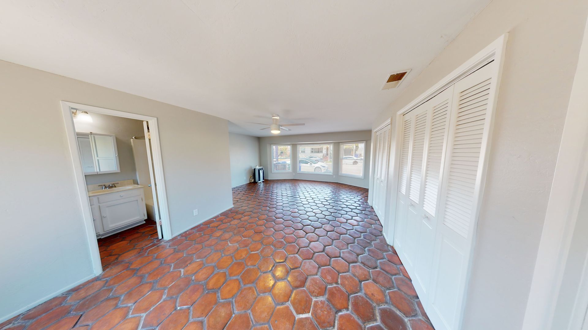 Interior view of a room with terracotta-tiled floor, windows, and a bathroom doorway.