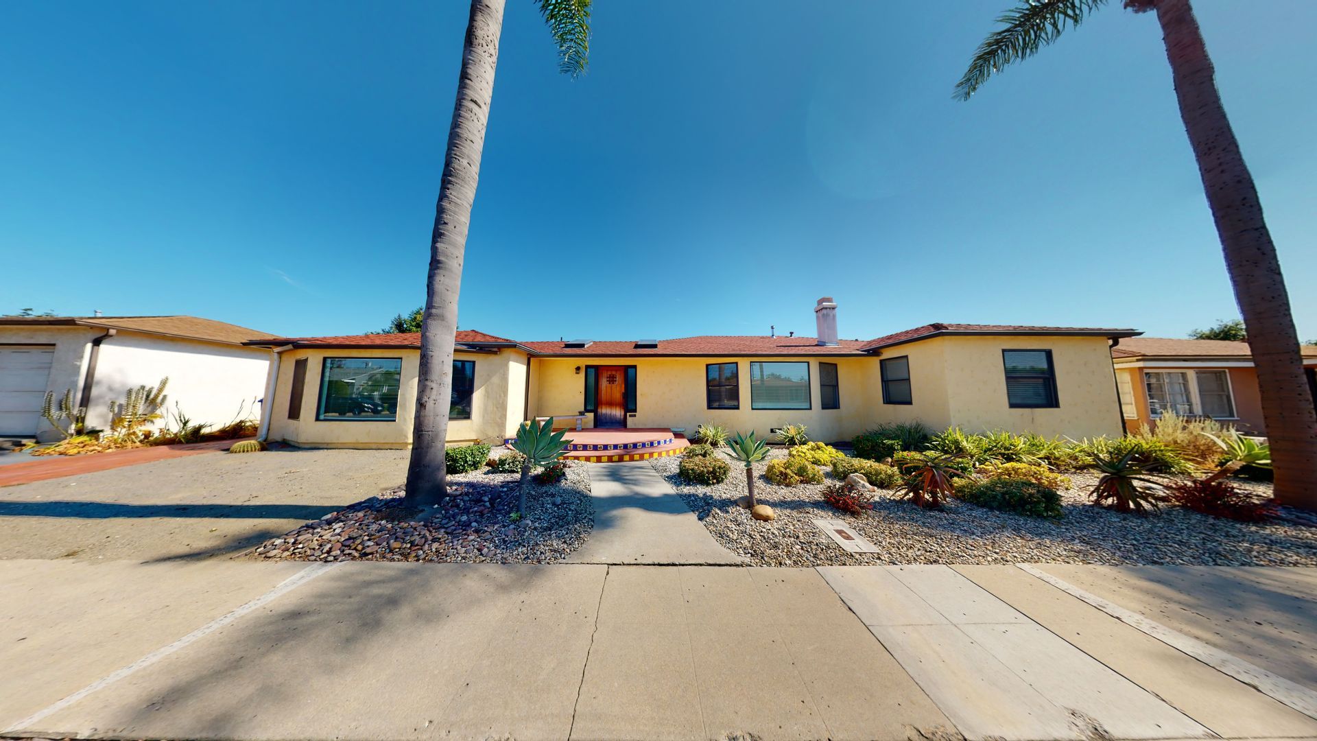 Yellow ranch-style house with landscaping, palm trees, and blue sky.