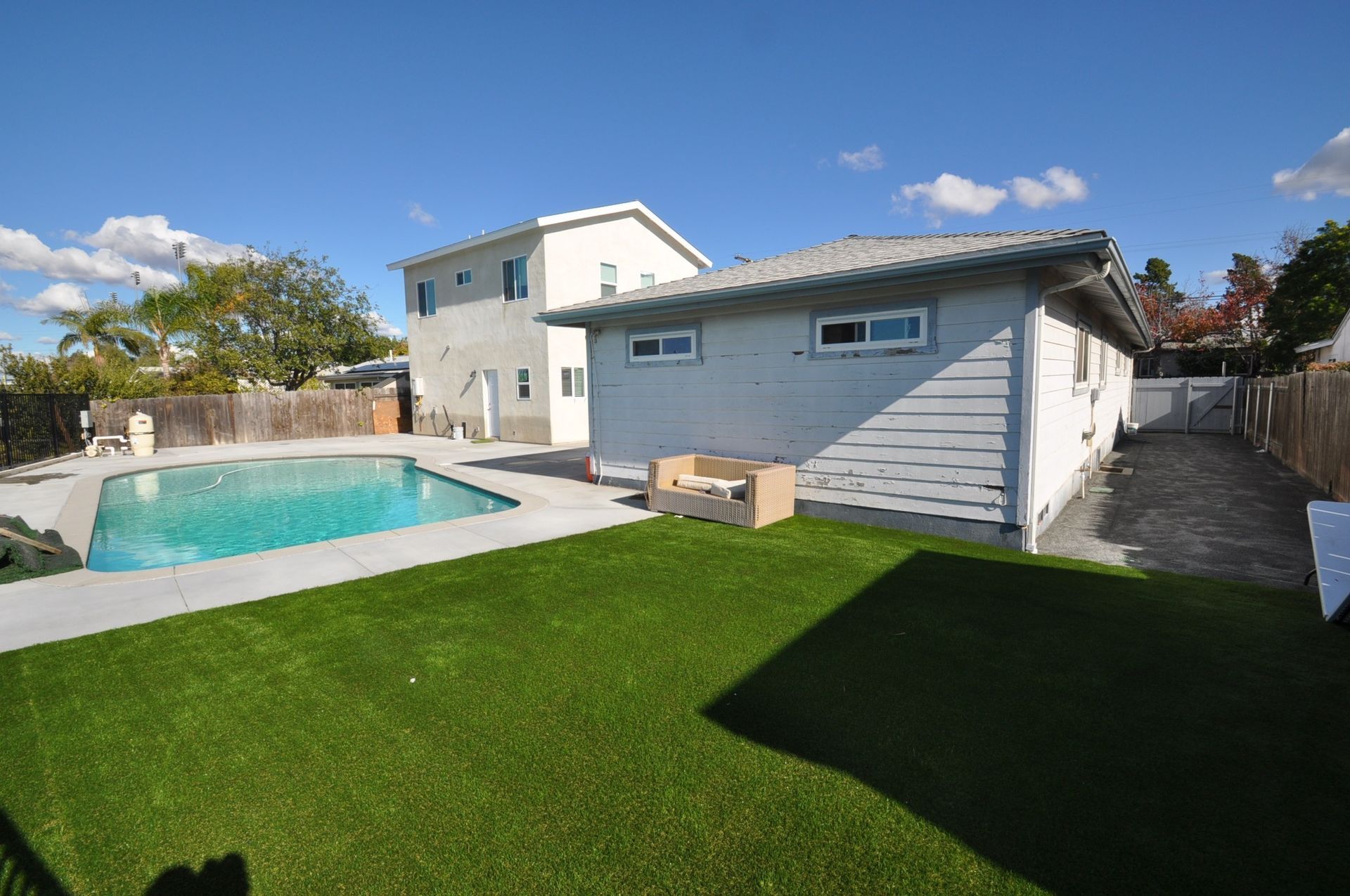 Backyard with pool, artificial grass, and two-story house on a sunny day.