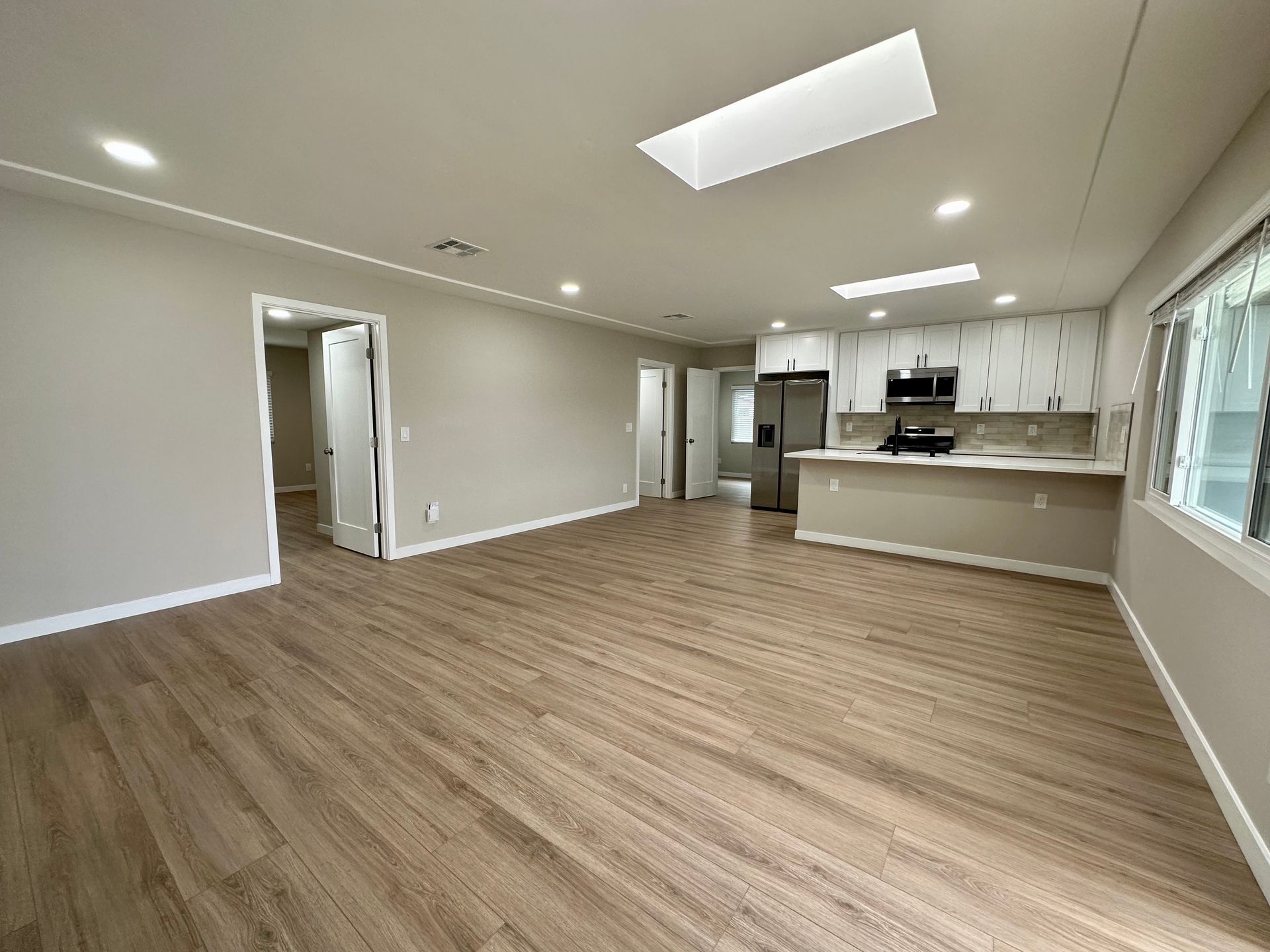 Open-concept living space with kitchen, neutral walls, light wood floors, and skylights.