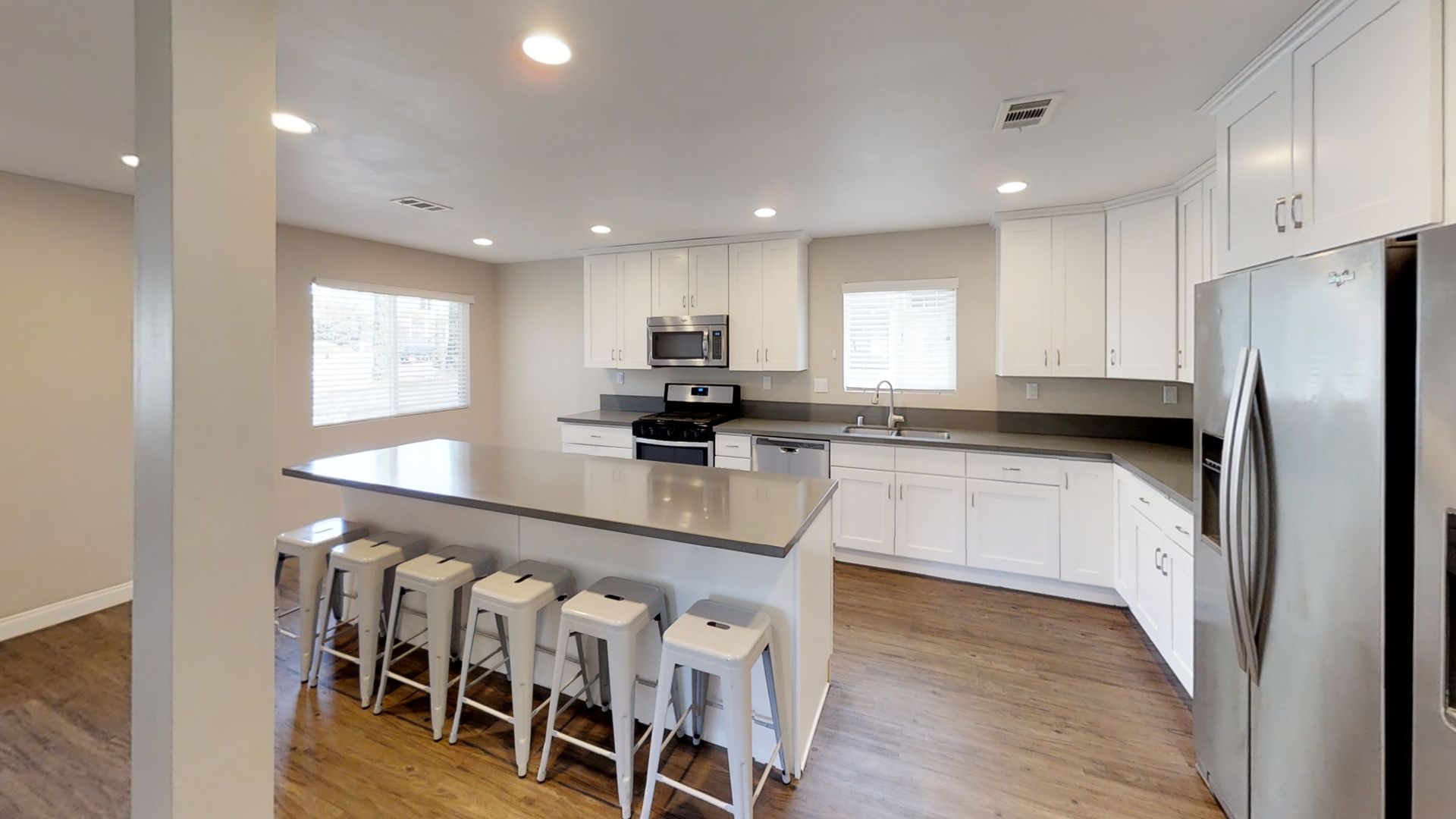 Spacious modern kitchen with white cabinets, stainless steel appliances, and a large island with bar stools.