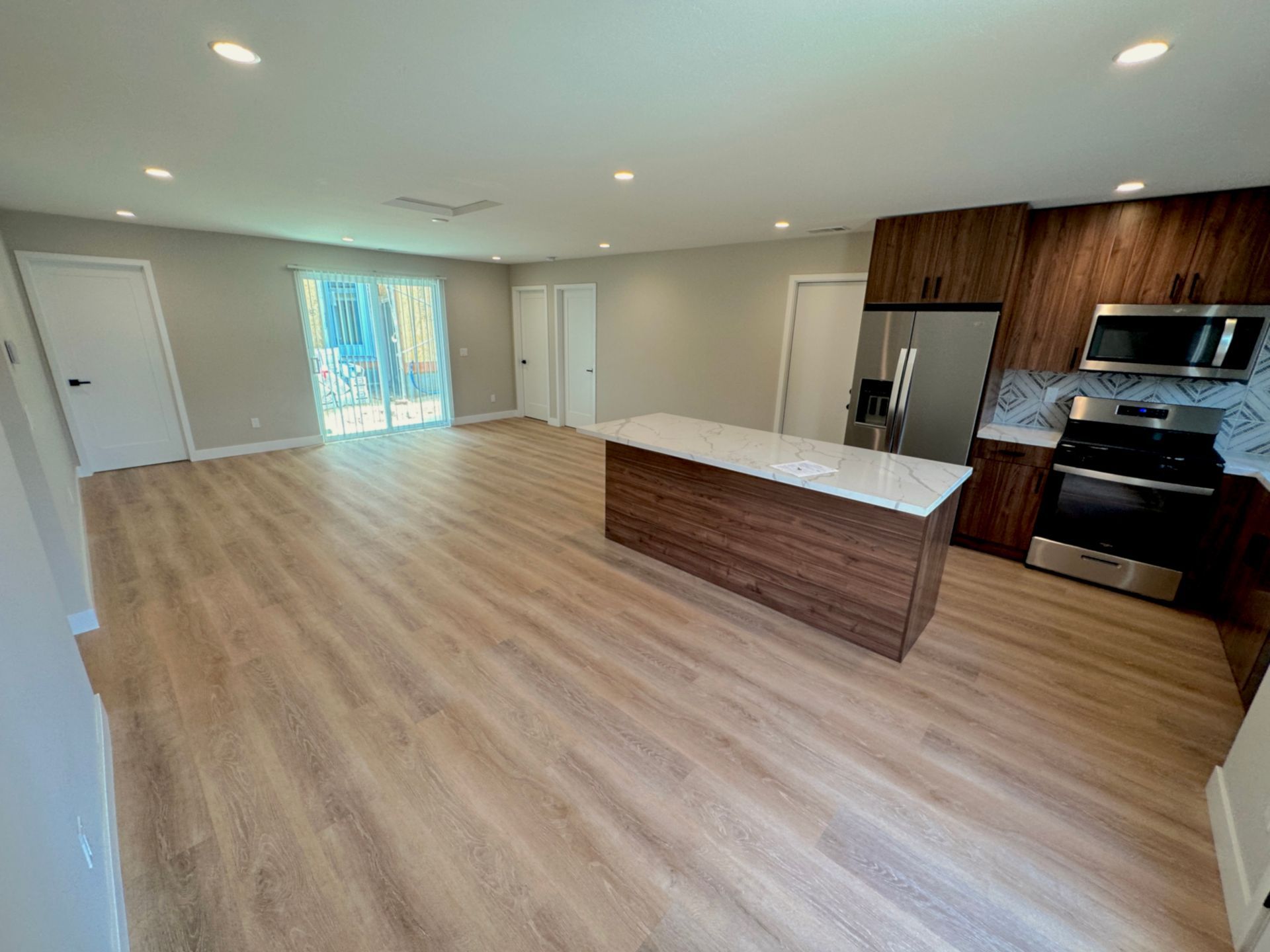 Spacious open-concept kitchen with wood floors, island, and dark wood cabinets; sliding glass door to outside.