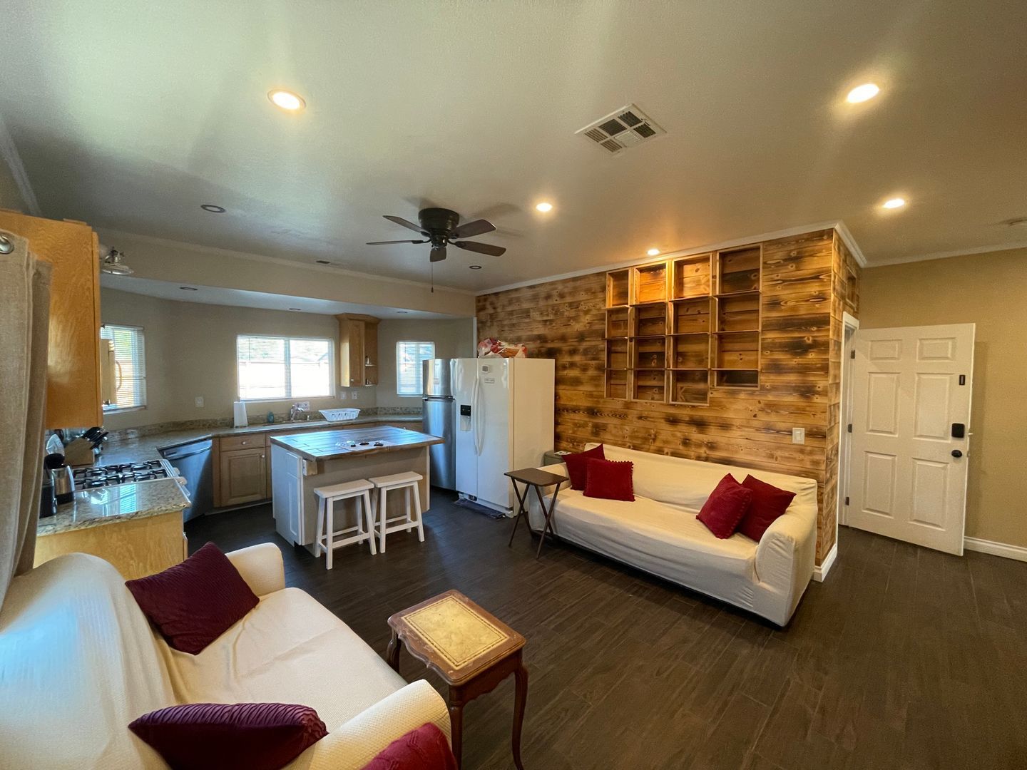 Open-concept living space: kitchen, two couches, wood accent wall, white appliances, dark wood floor.