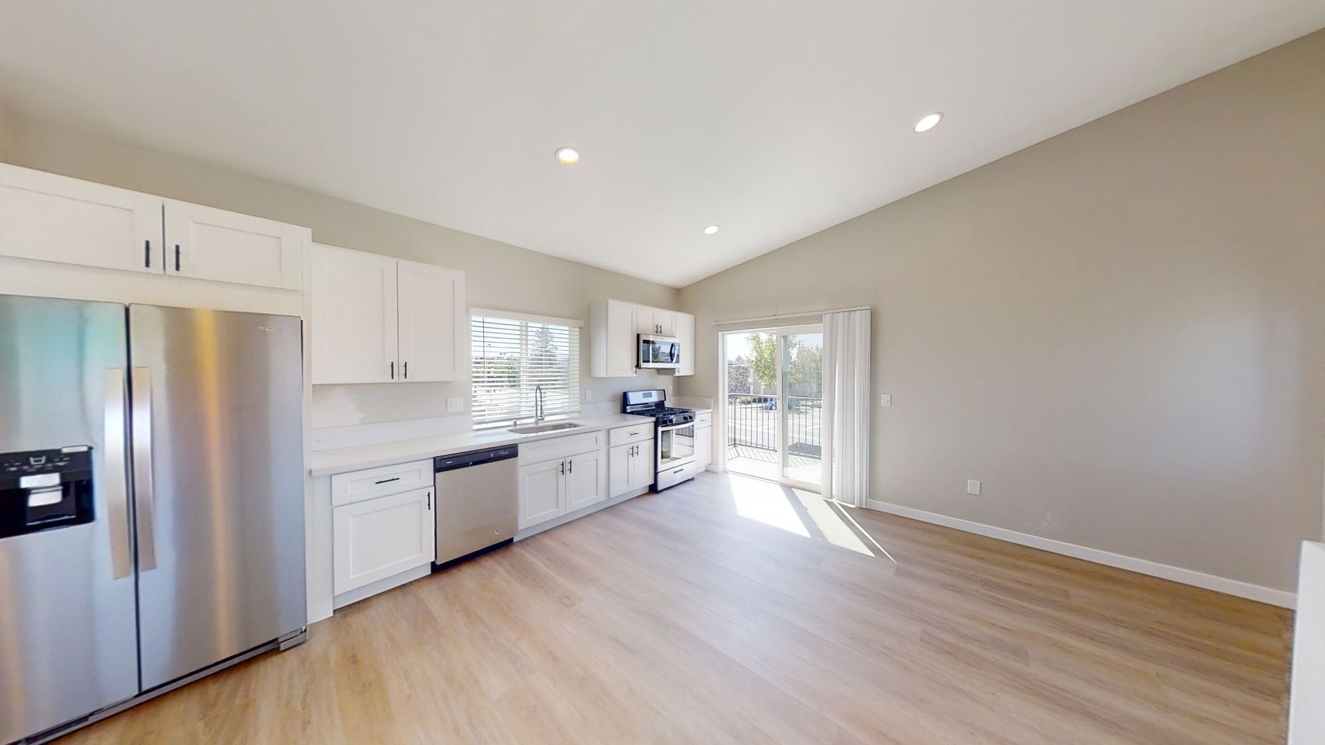 A modern kitchen with white cabinets, stainless steel appliances, and light wood flooring.