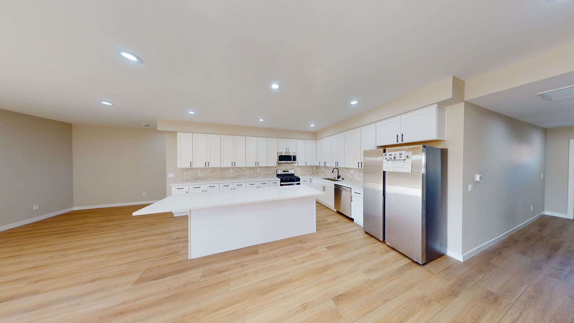 Modern kitchen with white cabinets, island, stainless steel appliances, and light wood floors.