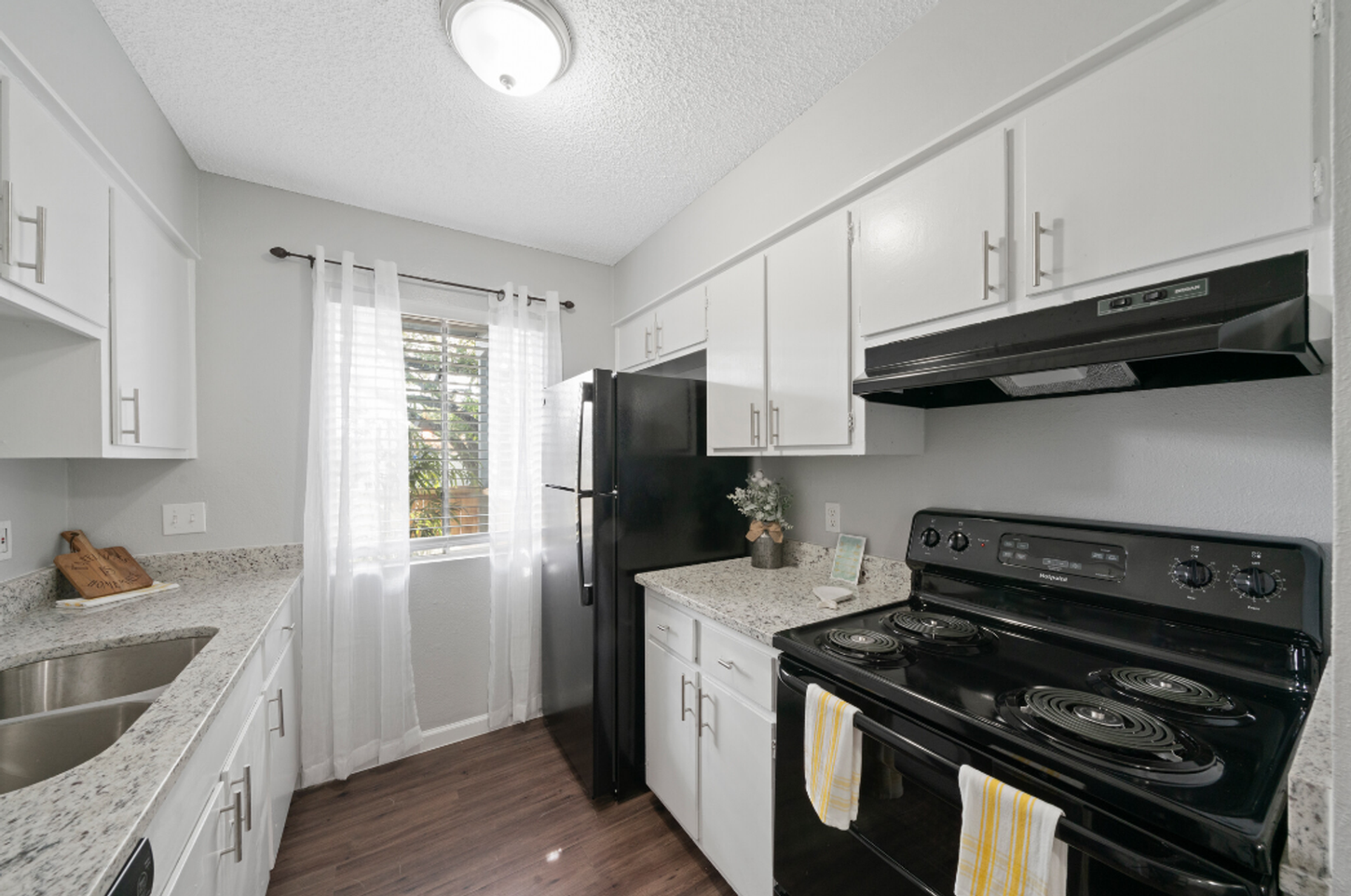 A kitchen with white cabinets , a black stove , a black refrigerator , and a sink.