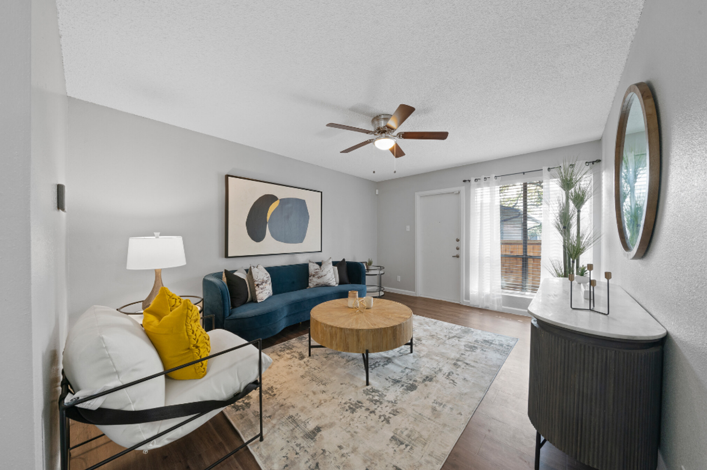 A living room with a blue couch , a coffee table , a mirror and a ceiling fan.