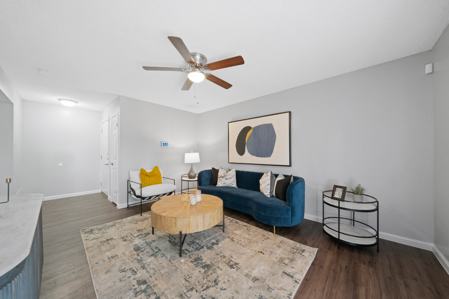 A living room with a couch , chair , coffee table and ceiling fan.