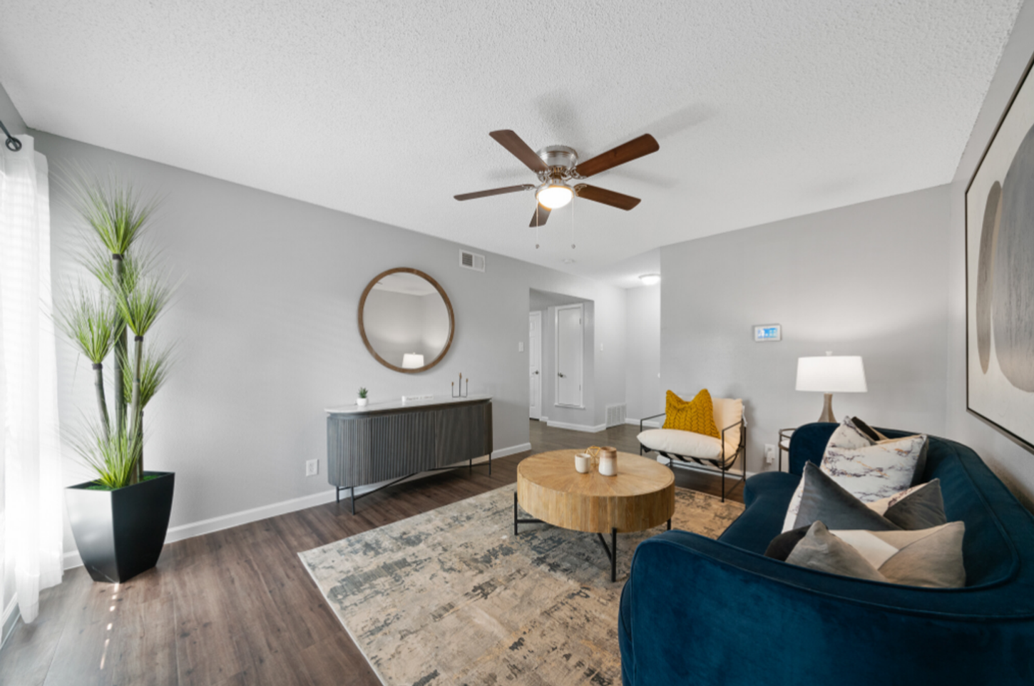 A living room with a blue couch , chair , coffee table and ceiling fan.