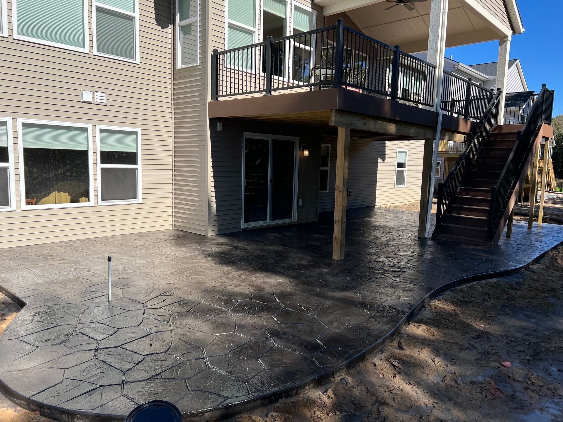 Concrete patio with dark tree bark pattern, beneath a home with a deck and stairs.