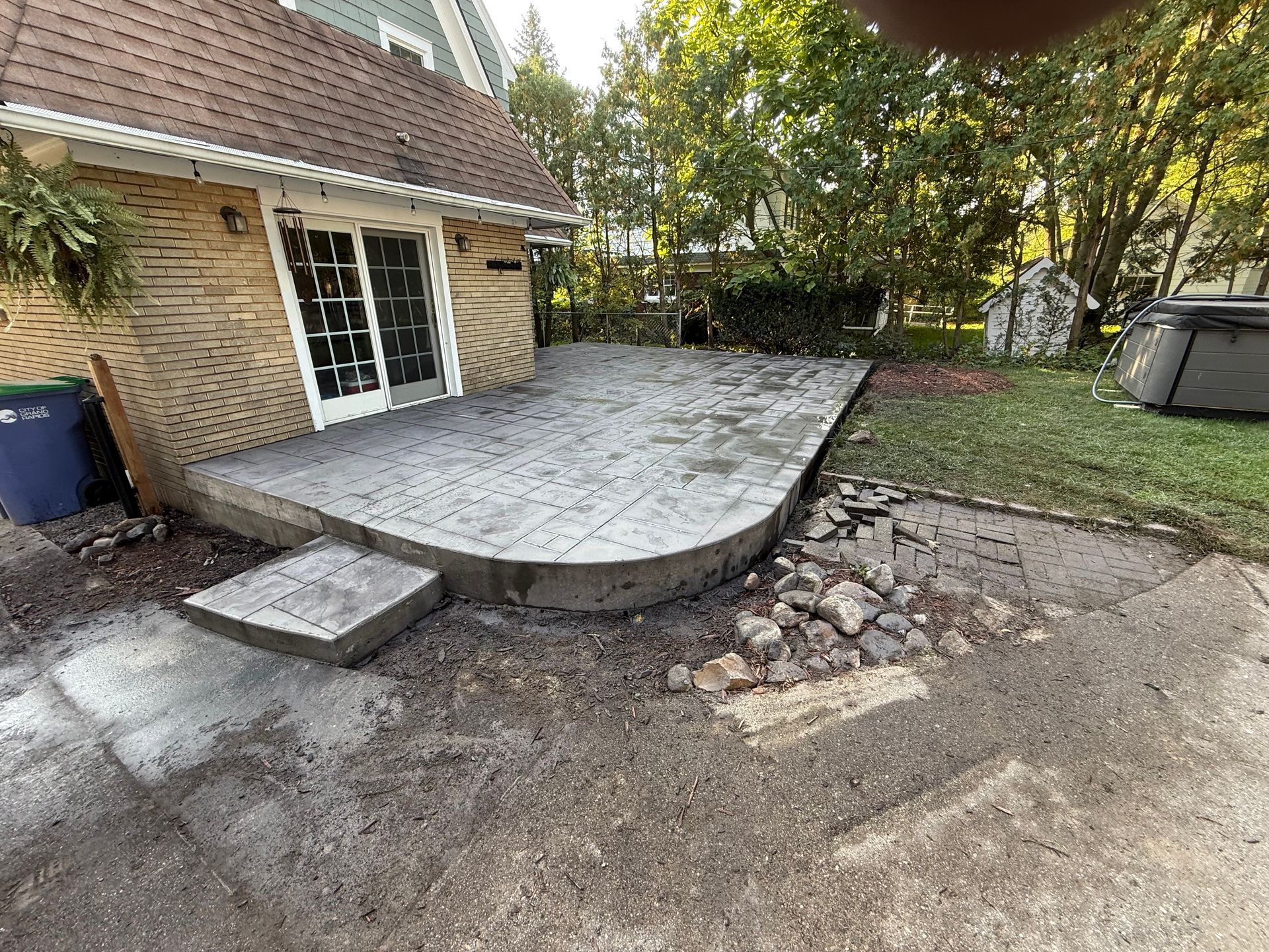 Newly constructed concrete patio next to a house with a curved edge and a separate step.