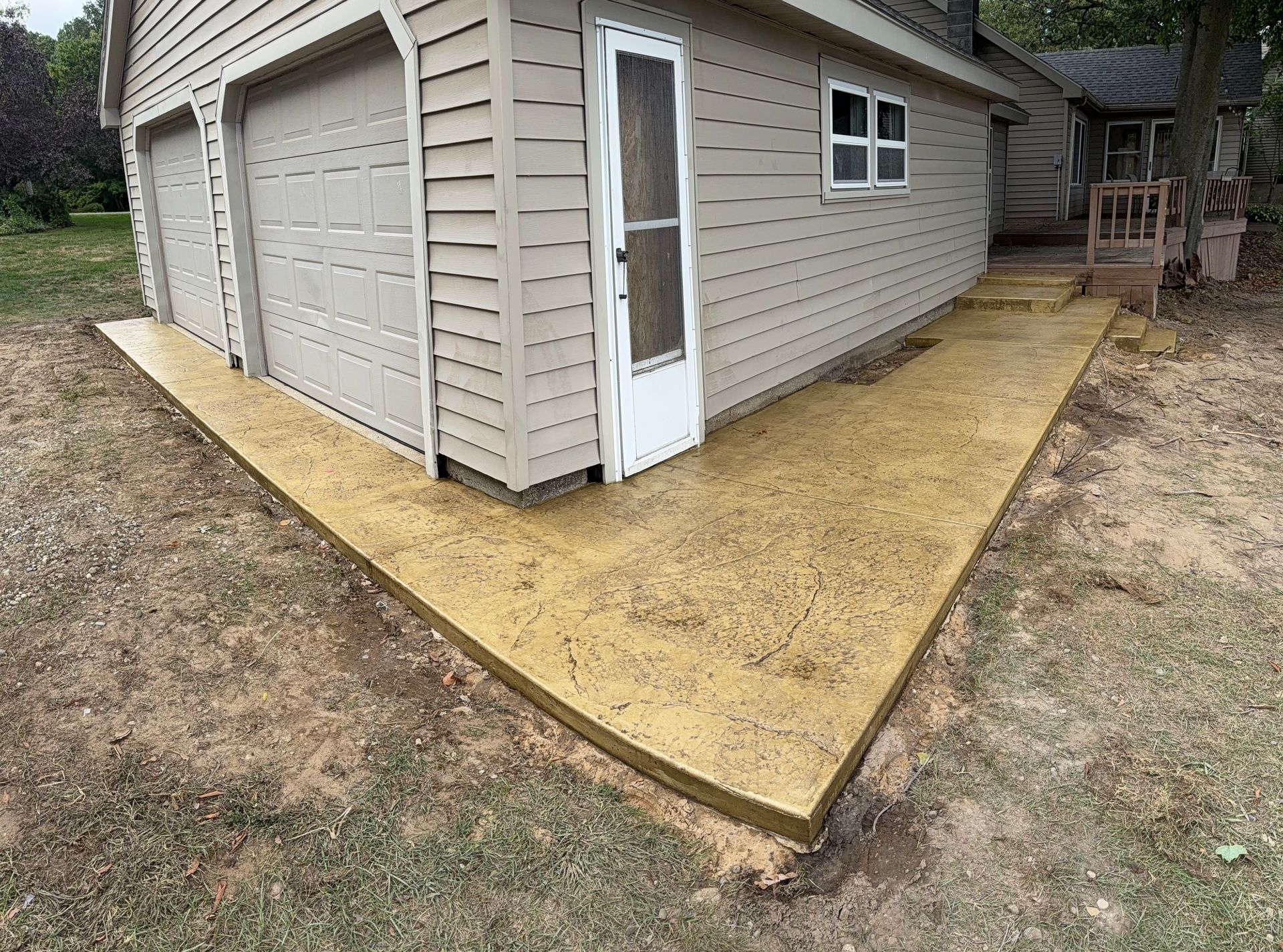 Yellow concrete pathway leading to a garage door and side door. Light-colored siding.
