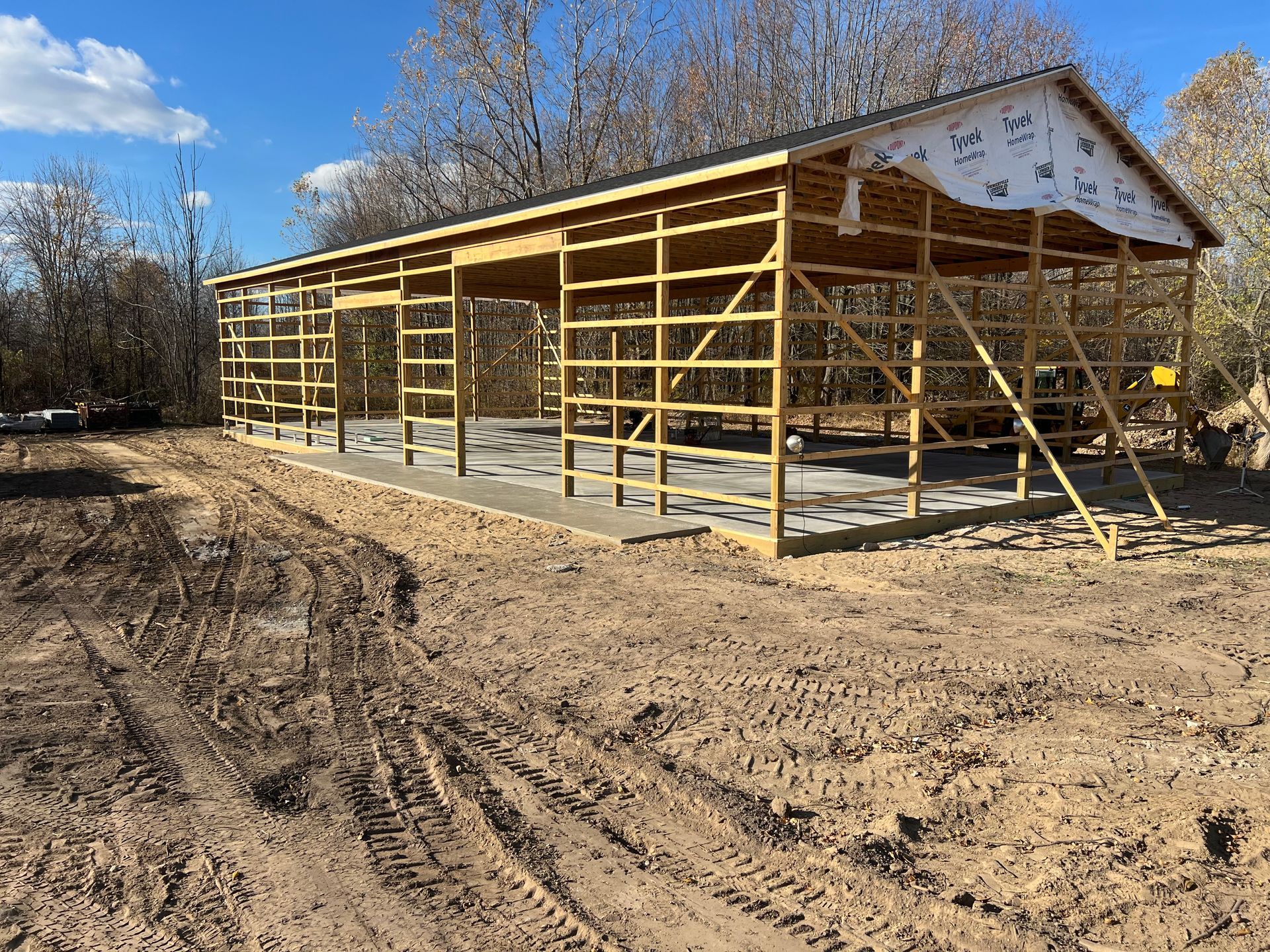 Construction of a wooden framed building with concrete foundation on dirt ground. Blue sky in the background.