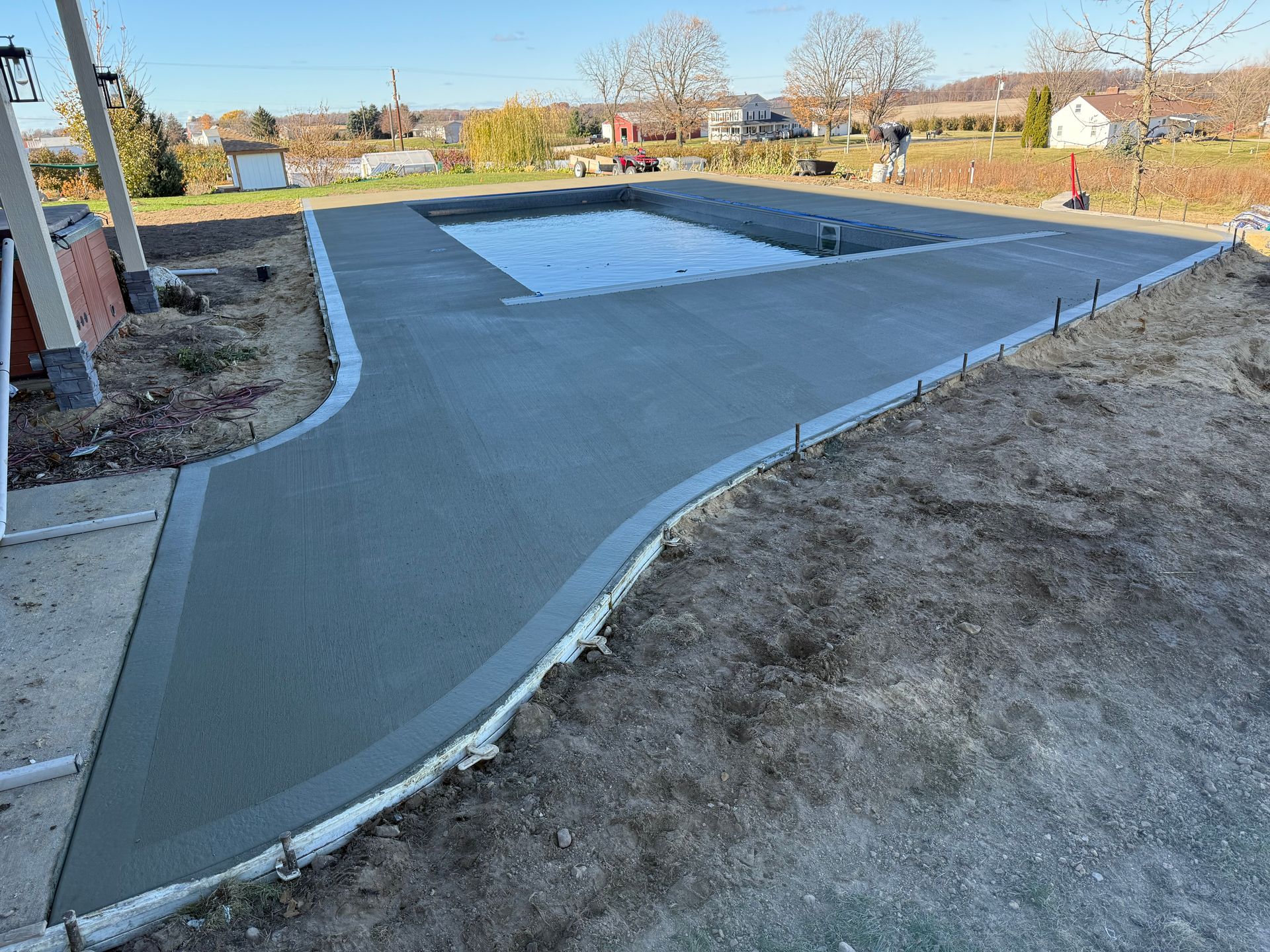 Freshly poured concrete around a rectangular swimming pool, outdoors.