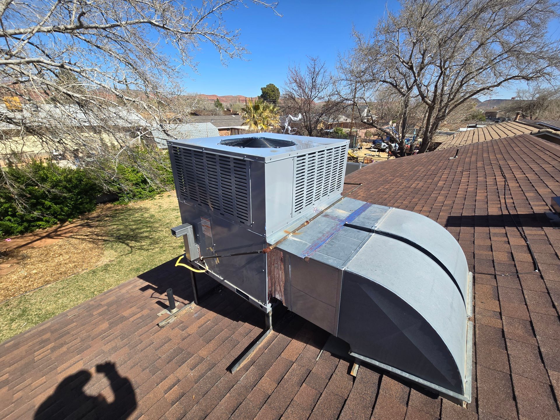 HVAC unit on a brown shingled roof on a sunny day.