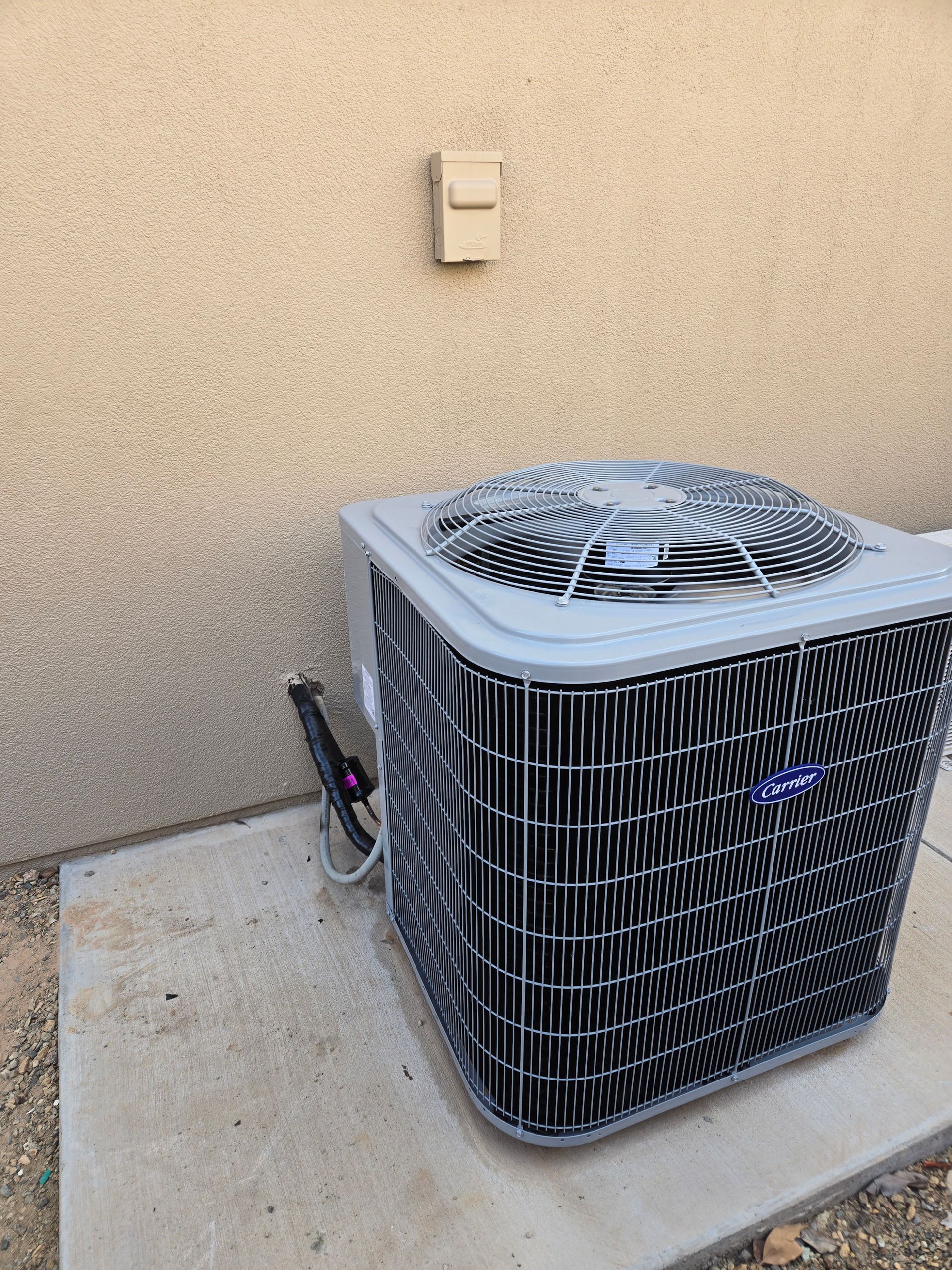 Air conditioning unit next to a tan wall with a small electrical outlet.