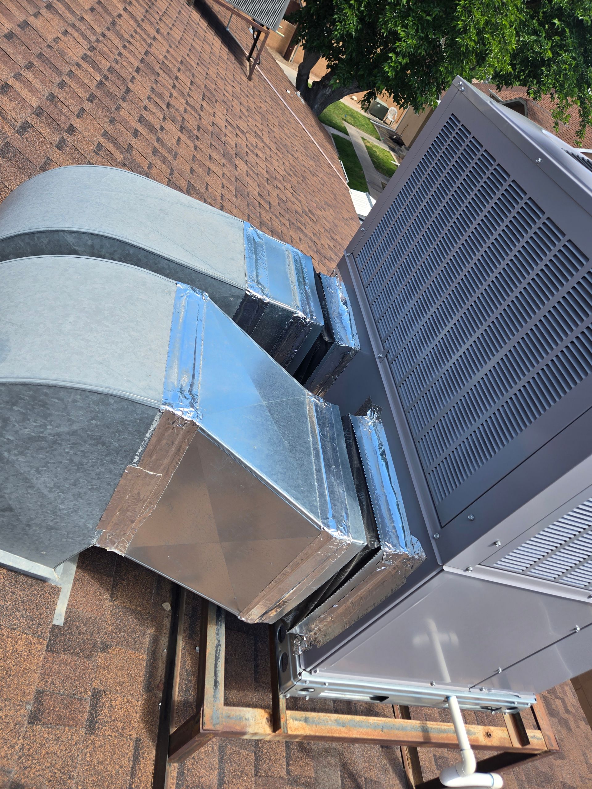 HVAC unit on a brown shingle roof, with metal ductwork.