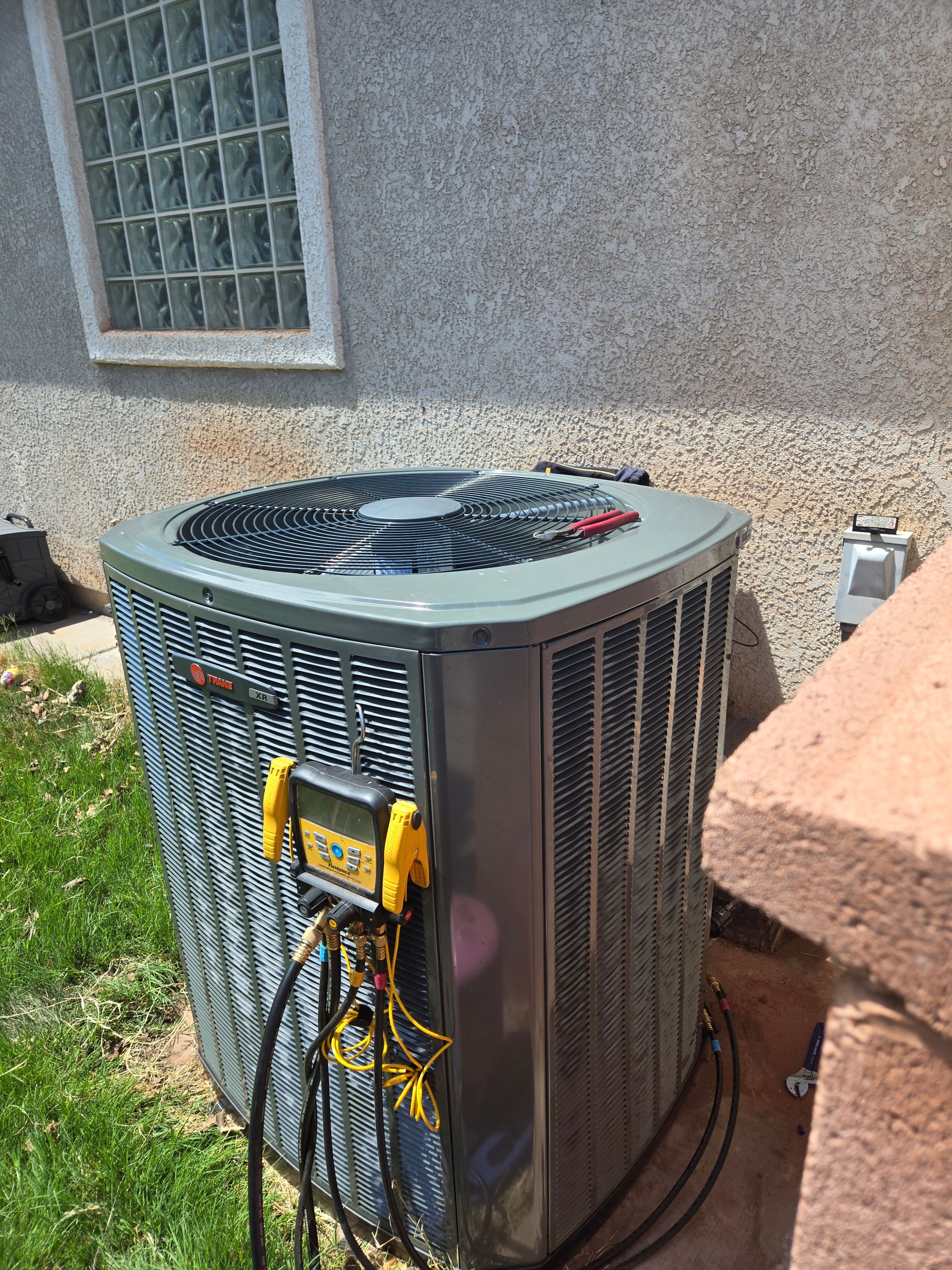 Air conditioner unit with diagnostic equipment, outside next to a wall and bricks.