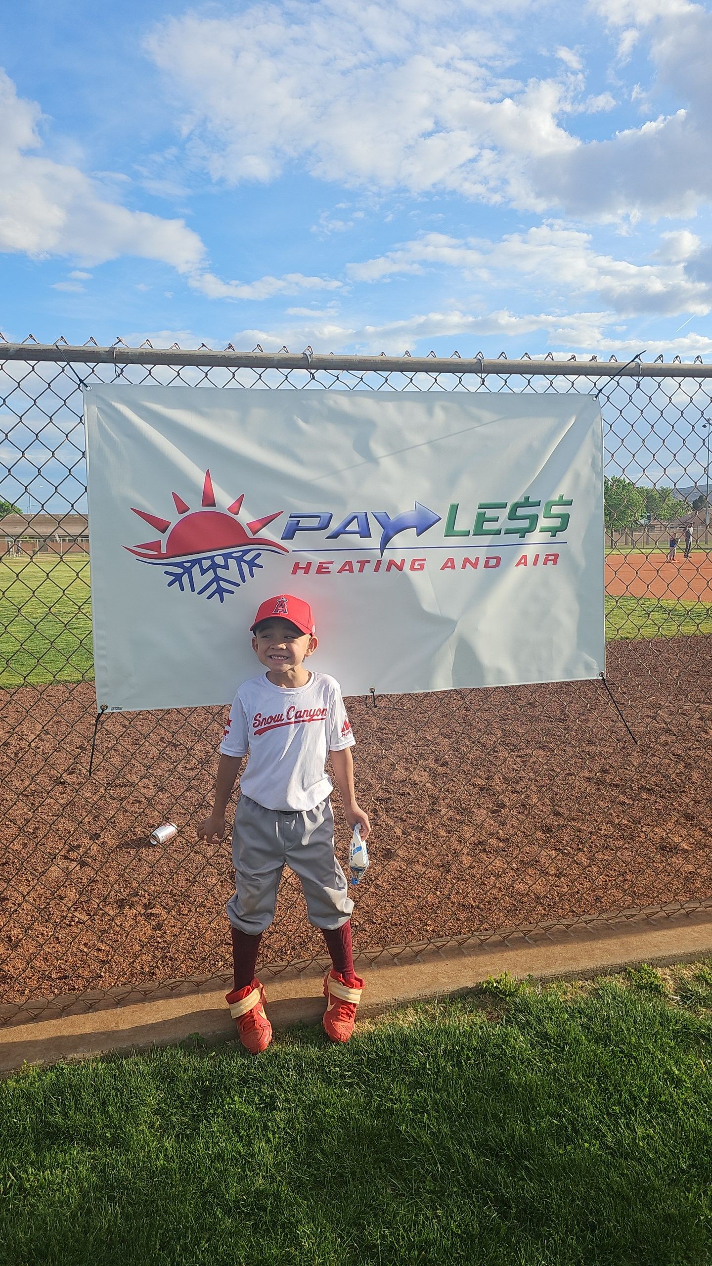 Boy in baseball uniform stands in front of a fence with a 