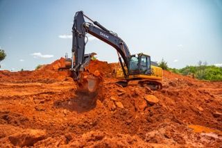 Excavator digging orange soil on a construction site under a blue sky.