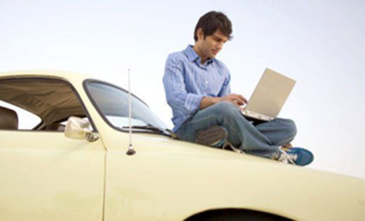 a man is sitting on top of a car using a laptop