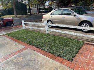 A car is parked in a driveway next to a white fence.