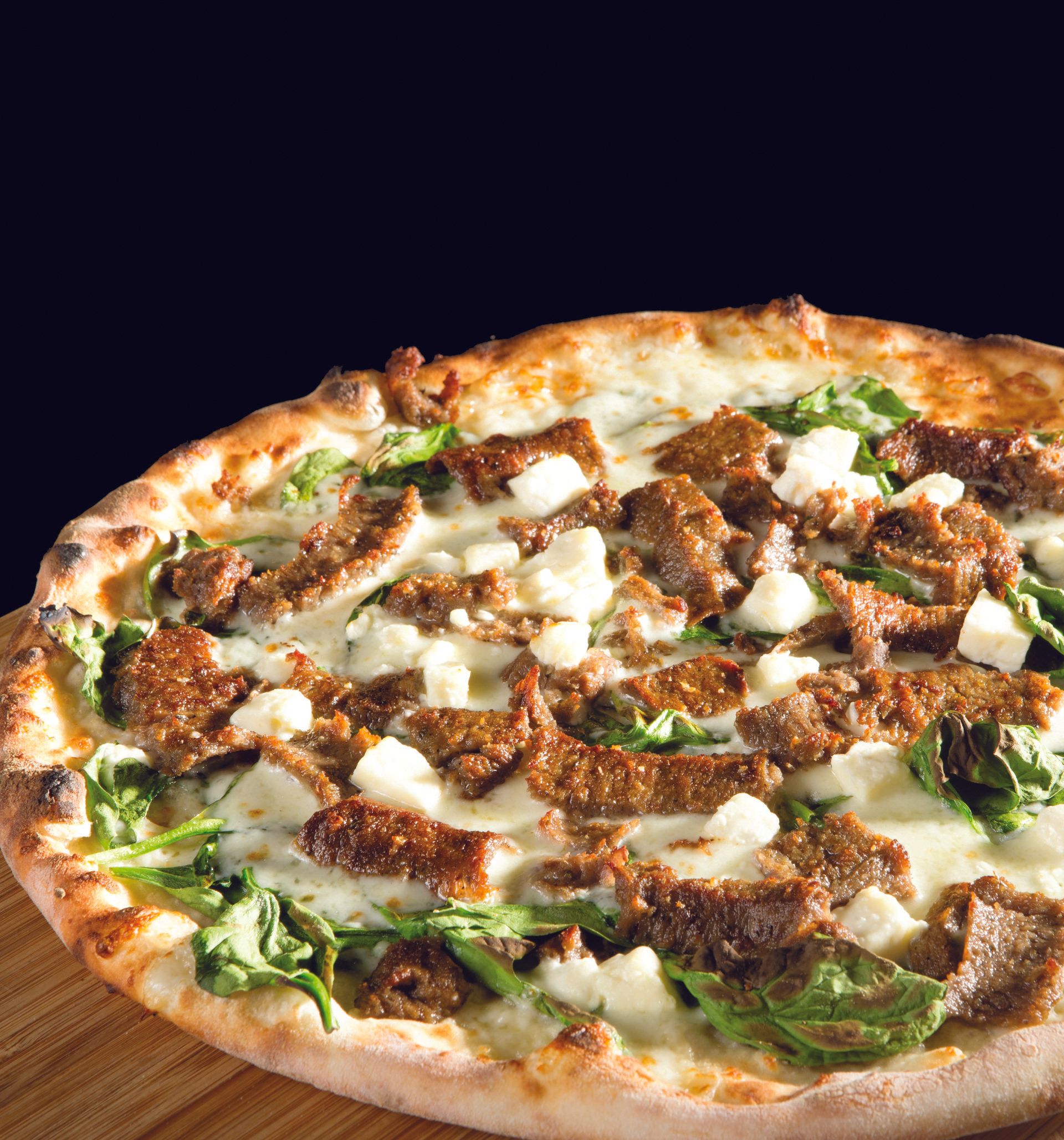 A pizza with meat cheese and spinach on it