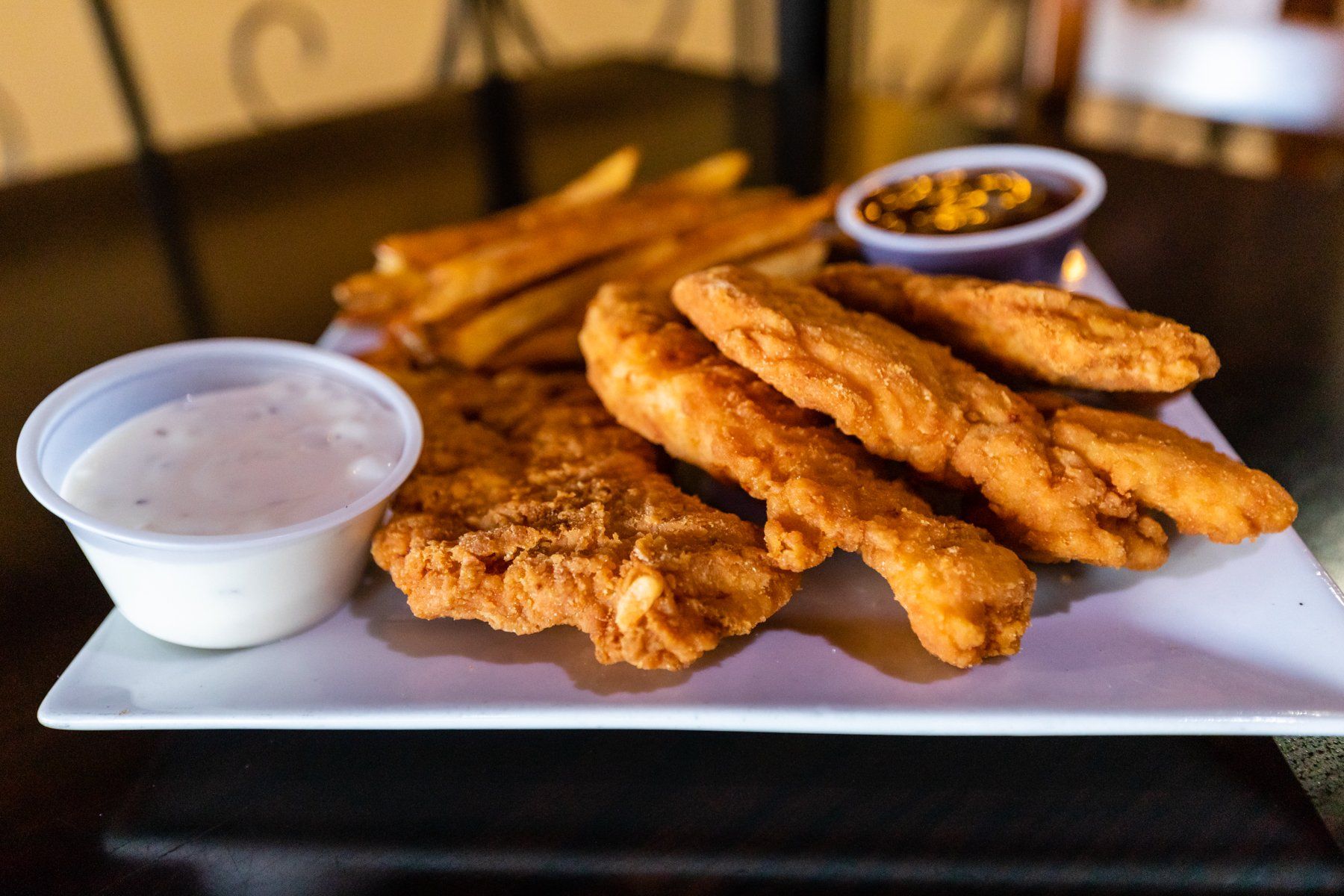 A plate of fried chicken and french fries with dipping sauces